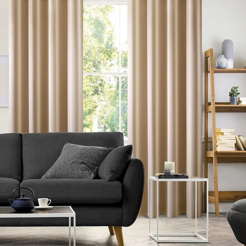 A dark gray sofa stands in front of tall beige curtains next to a wooden ladder bookshelf in a modern living room.