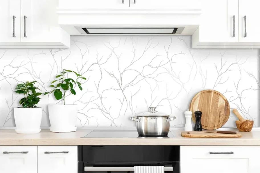 A modern white kitchen features shaker-style cabinets, a light wood countertop, a black stovetop, and a backsplash with a gray branch pattern.
