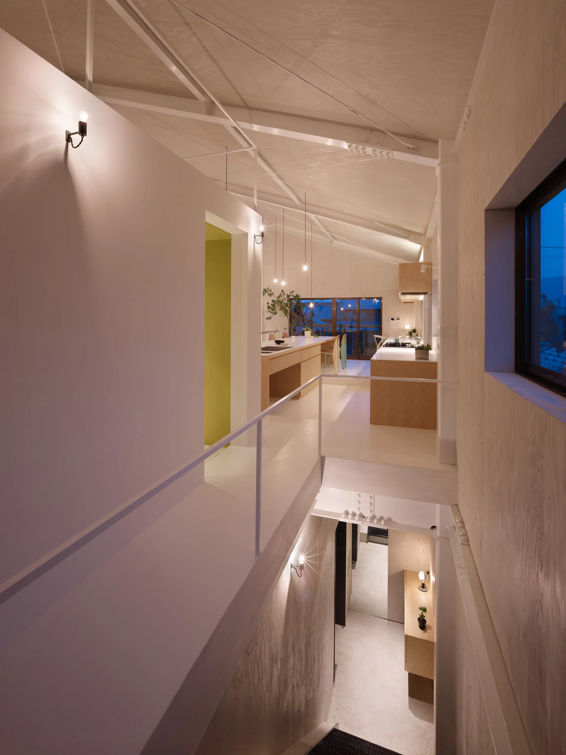A multi-level modern interior featuring white exposed ceiling trusses, a kitchen island, and a staircase landing surrounded by plywood paneling.