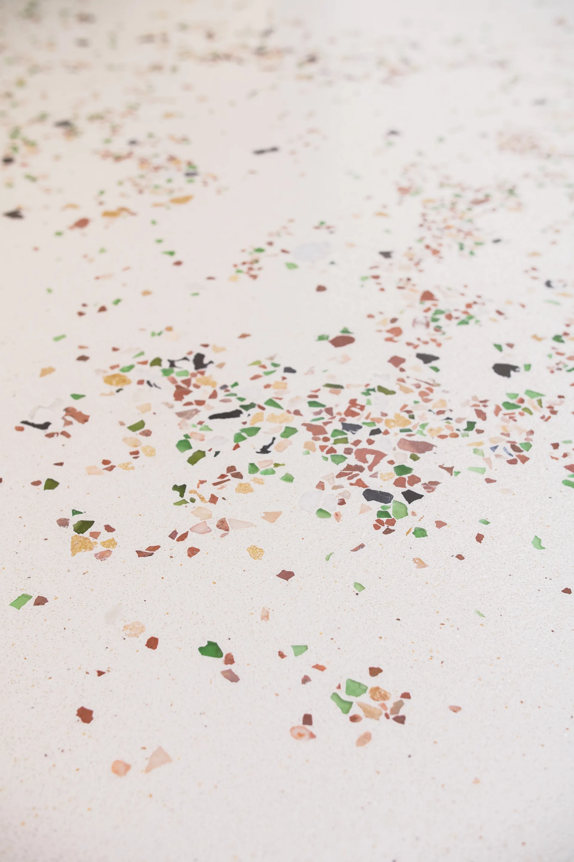 A close-up view of a cream-colored terrazzo surface featuring scattered green, brown, and ochre stone fragments.