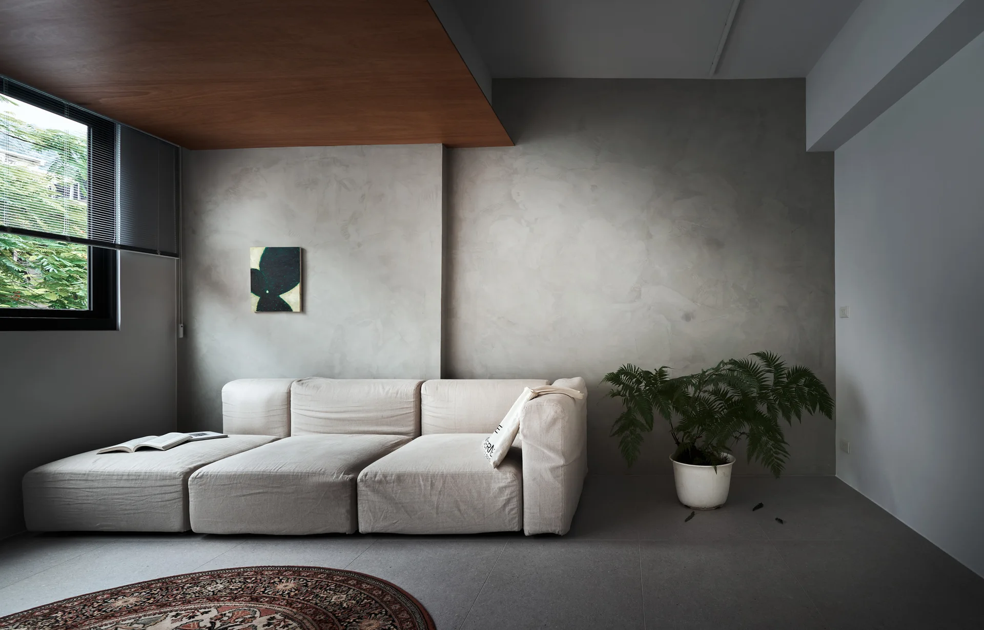 A cream modular sofa sits against a textured grey plaster wall beneath a wood-paneled ceiling section in a modern living room.