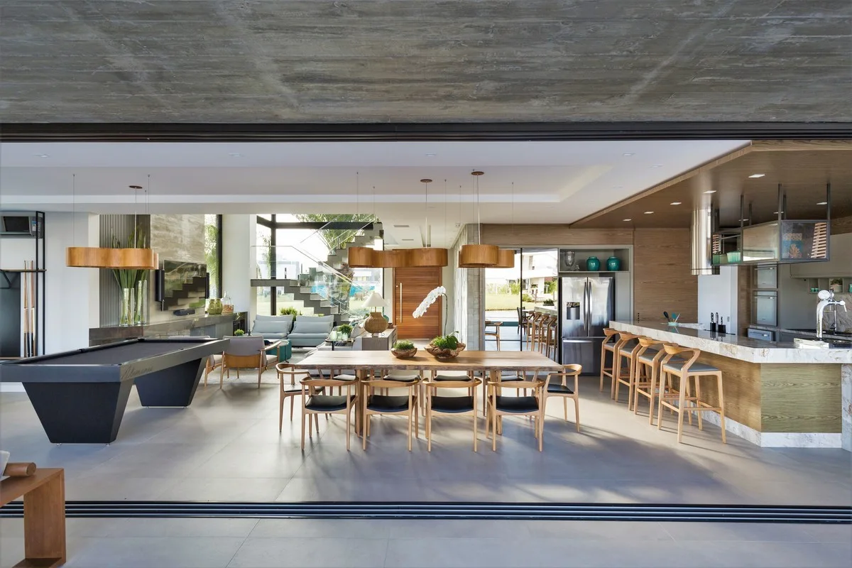 A spacious open-plan interior featuring an exposed concrete ceiling, a live-edge wood dining table, a black pool table, and a kitchen island.