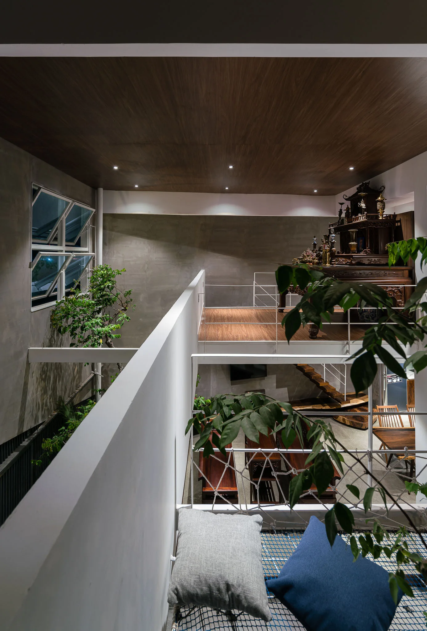 A multi-level interior features a blue mesh mezzanine floor with cushions overlooking a lower living area with wooden stairs and concrete walls.