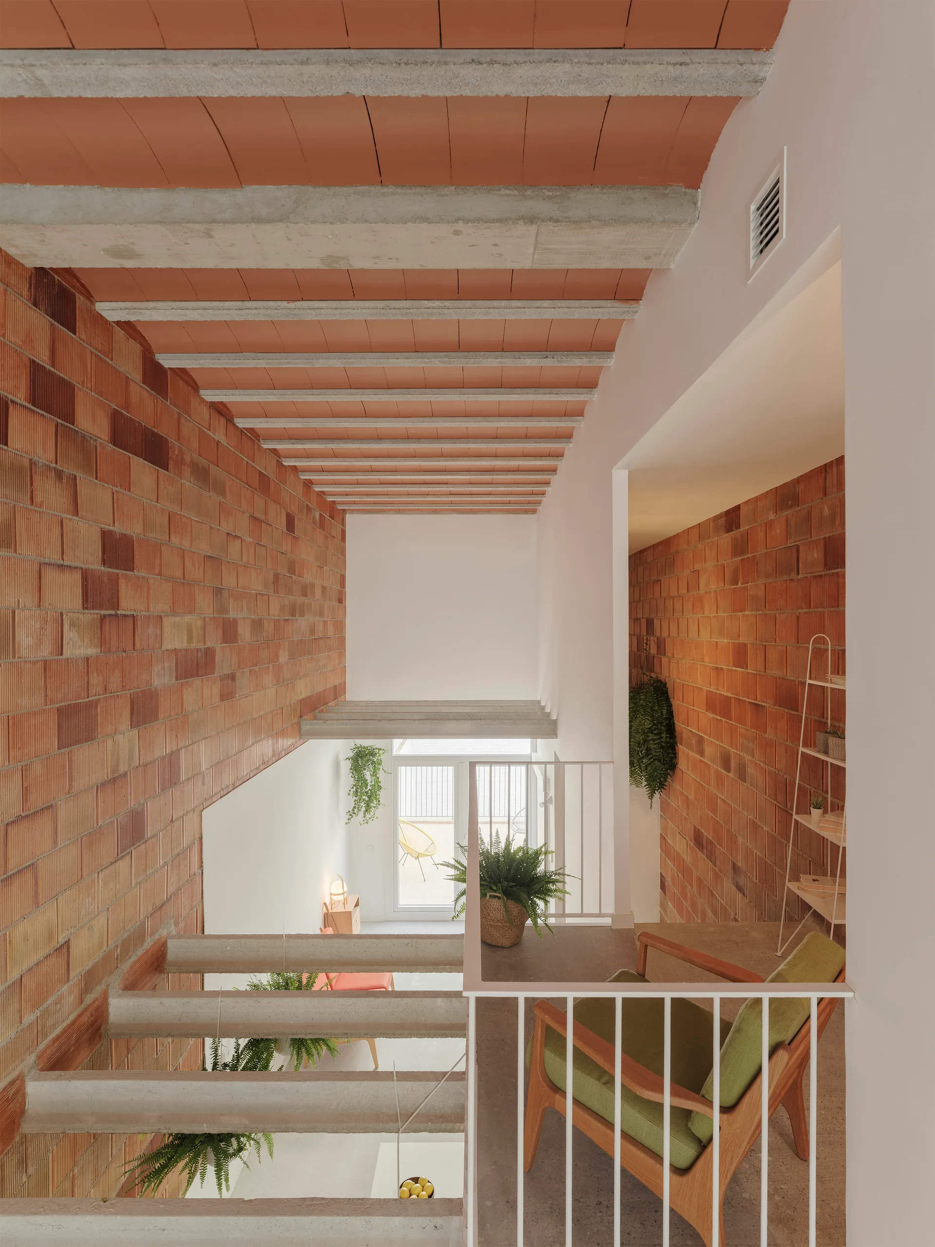 A high-angle view of a concrete staircase flanked by exposed brick walls under a ceiling of concrete beams and red terracotta tiles.