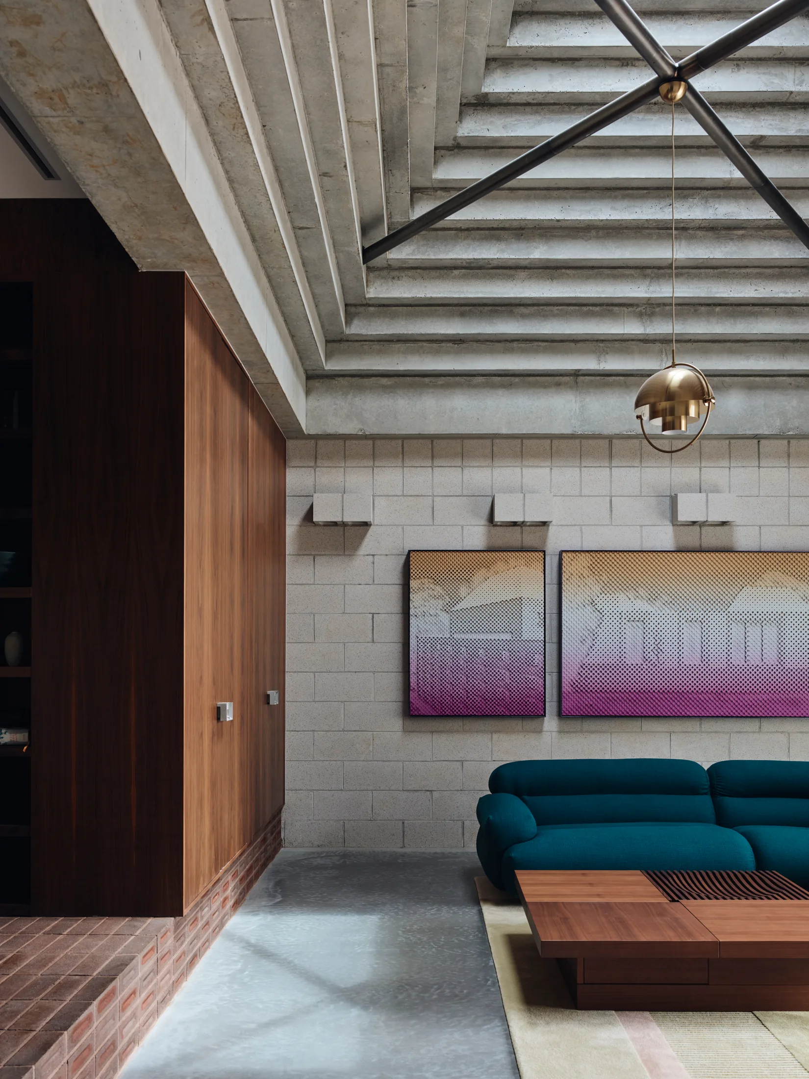 A modern living room featuring a tiered concrete ceiling, a light block wall, a teal sofa, and a wood cabinet unit on a brick base.