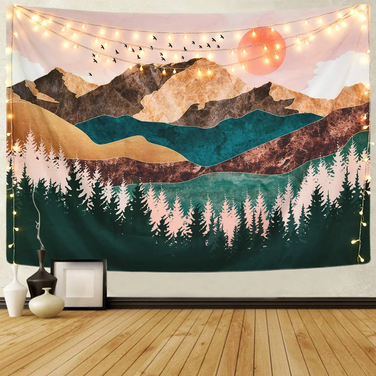A colorful mountain landscape tapestry hangs on a beige wall decorated with glowing string lights above light wood floors.