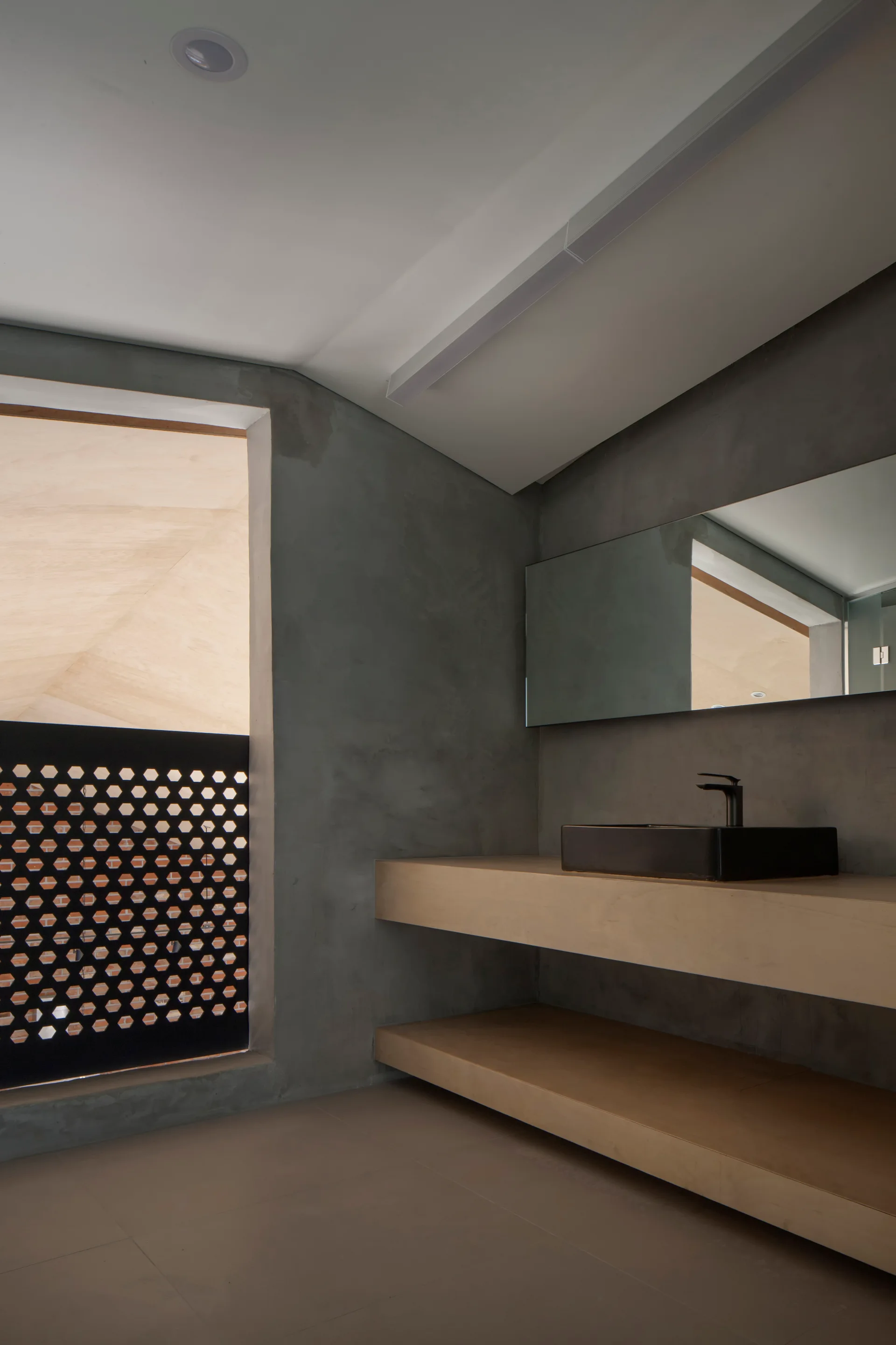 A minimalist bathroom features textured grey concrete walls, a double-tier floating wood vanity, a black vessel sink, and a rectangular mirror.