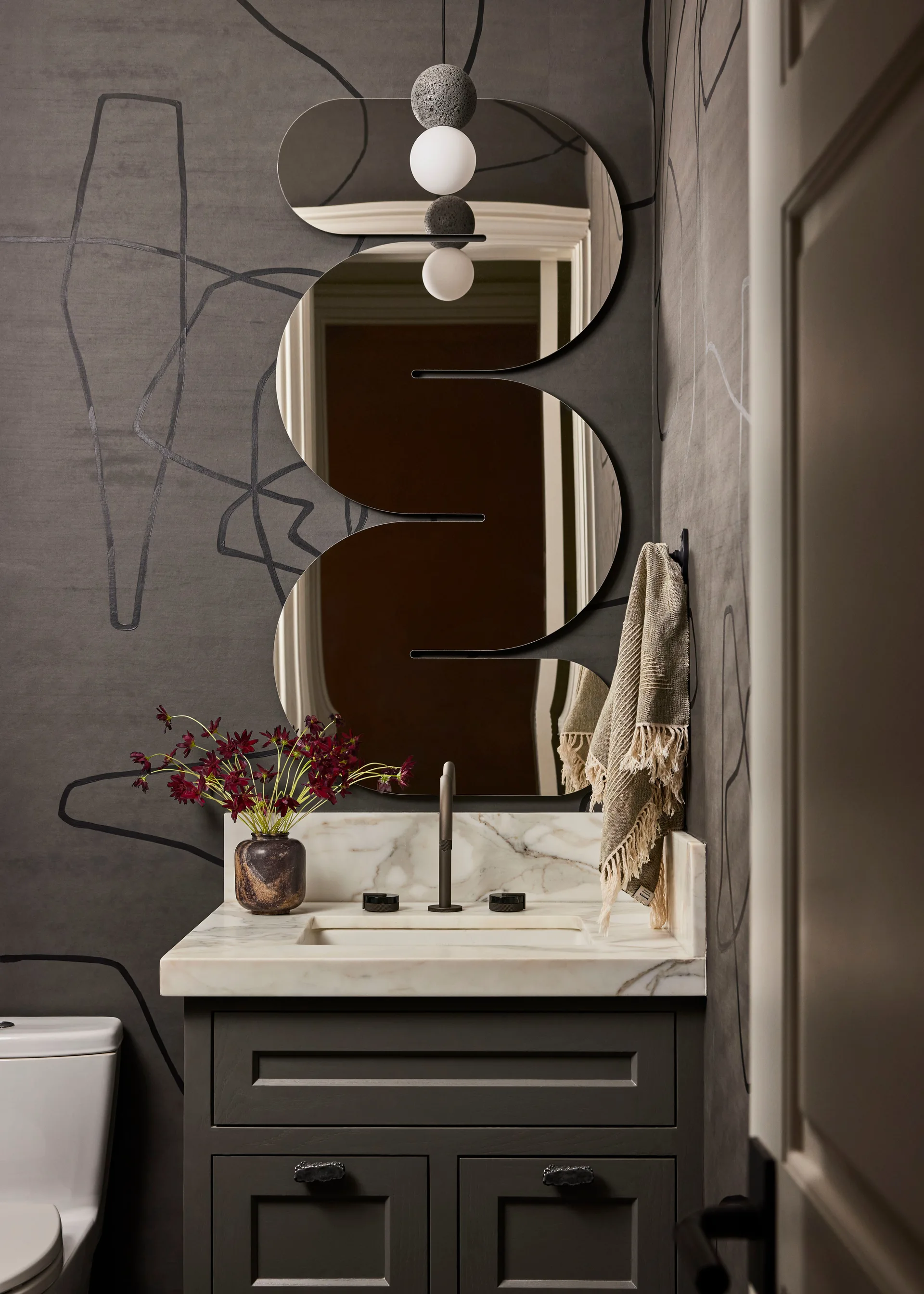 A charcoal grey powder room vanity with a marble countertop features a serpentine mirror set against black line-art wallpaper.