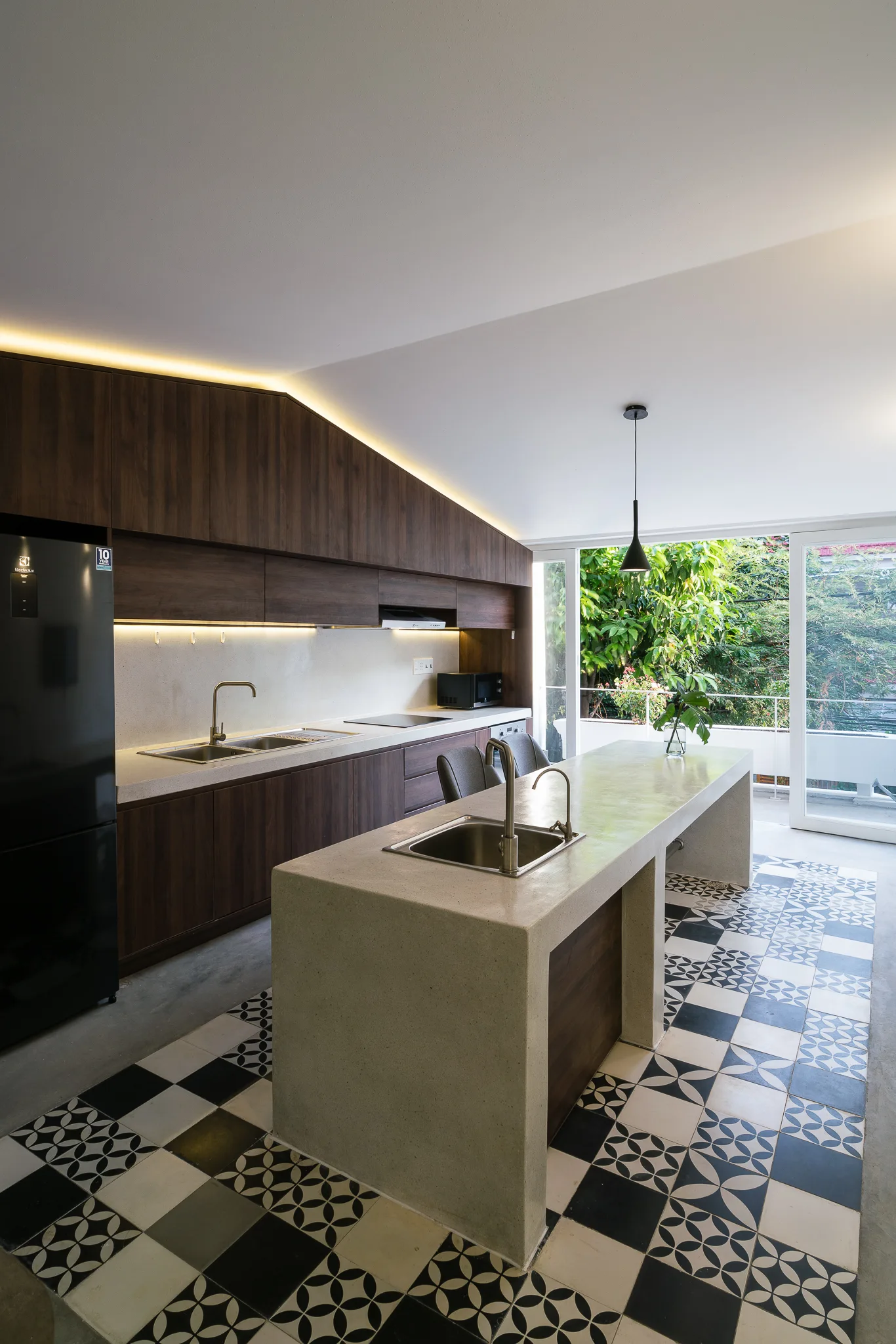 A modern kitchen featuring dark wood cabinetry, a concrete-style island with a sink, and a black-and-white geometric tiled floor.