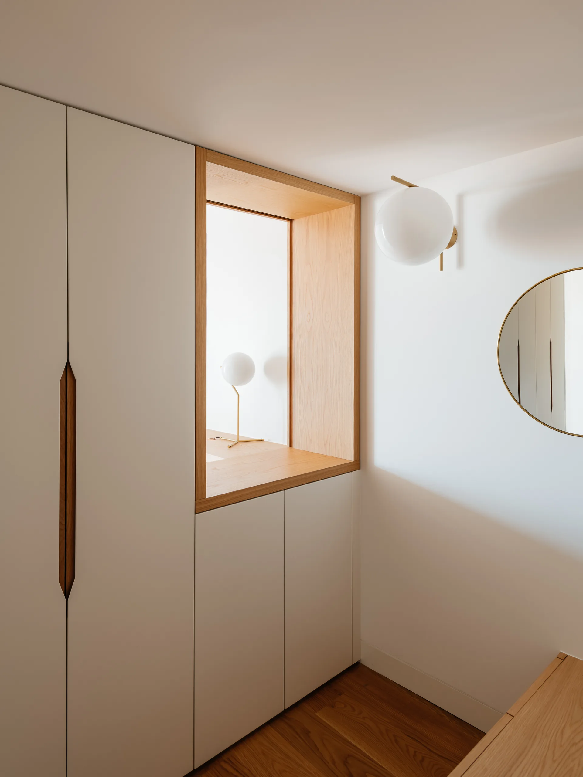 Matte off-white built-in cabinets feature a recessed light wood handle and a rectangular niche containing a small globe lamp next to a wall sconce.