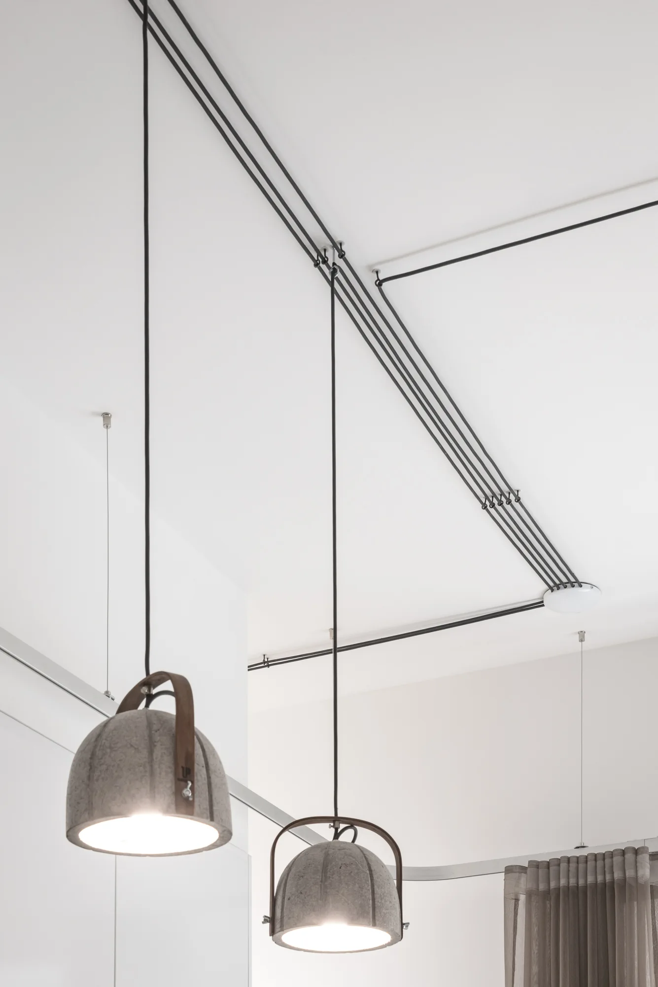 Two gray felt dome pendant lights hang from a white ceiling, with their black electrical cables organized into neat, geometric lines.