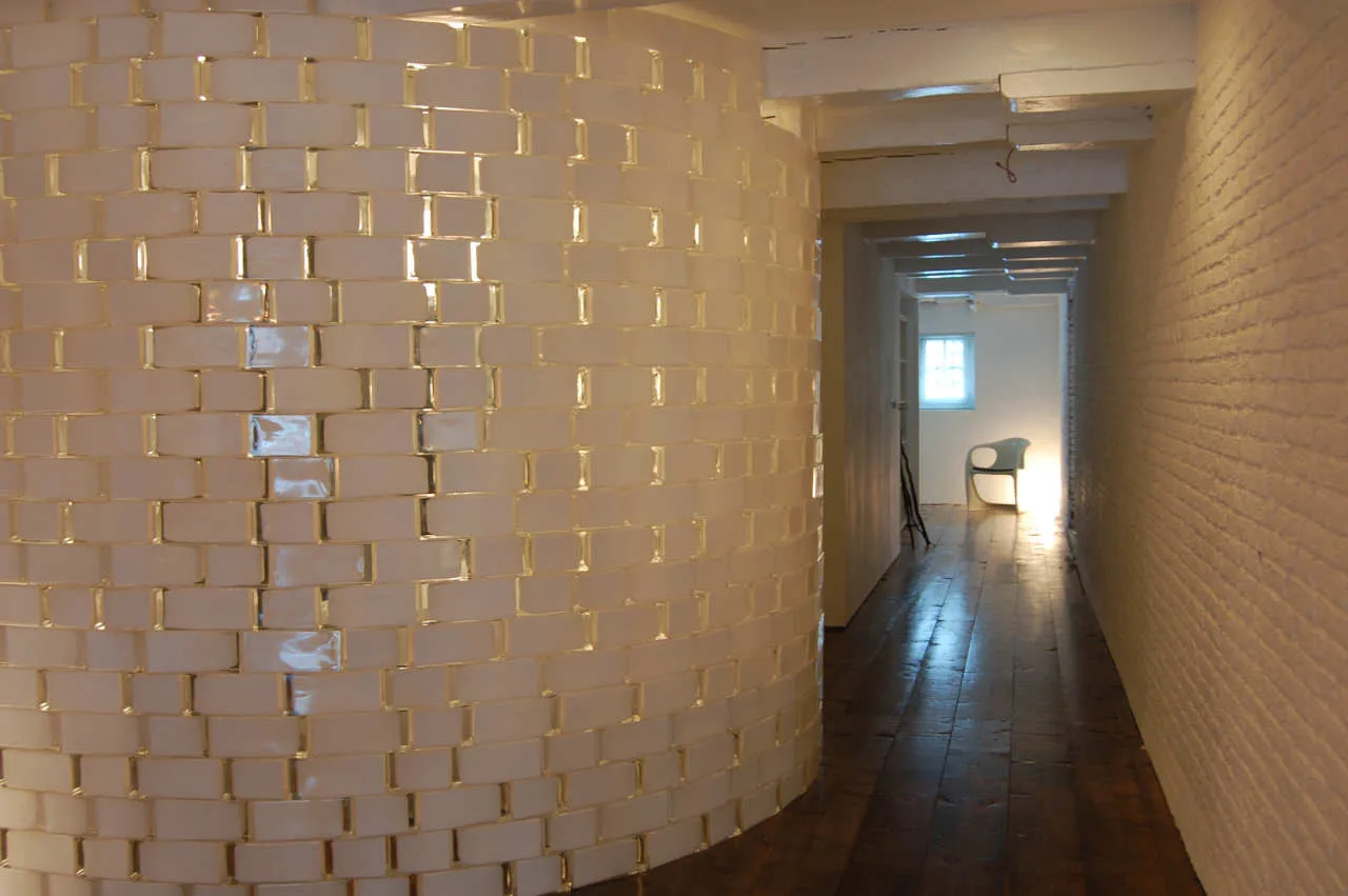 A narrow hallway features a prominent curved white brick partition wall, dark wood plank flooring, and exposed ceiling beams.