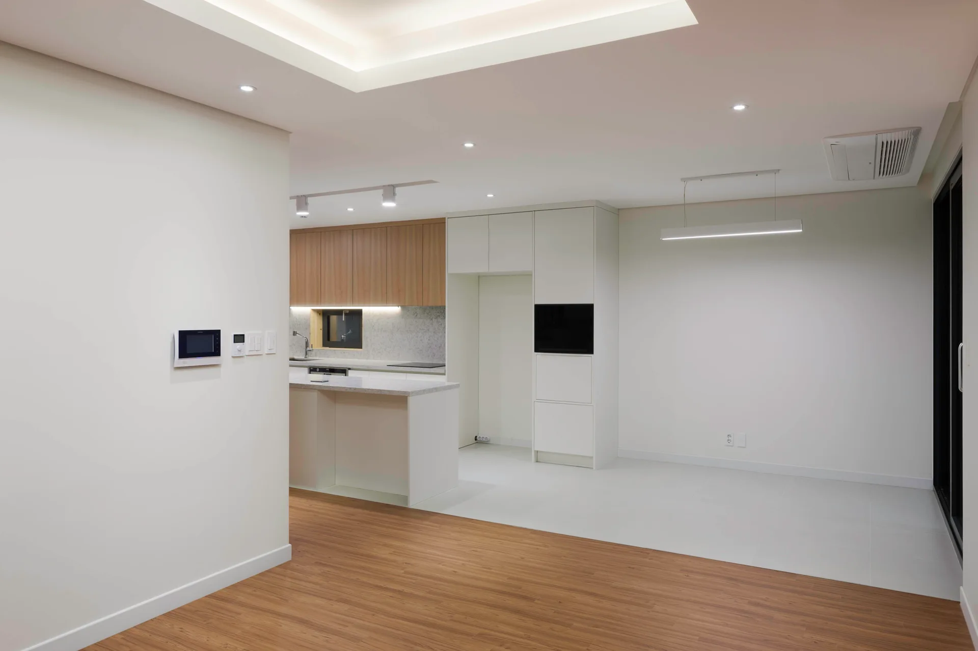 A minimalist open-plan kitchen featuring two-tone white and wood cabinets, an island, light grey tile flooring, and wood plank floors.