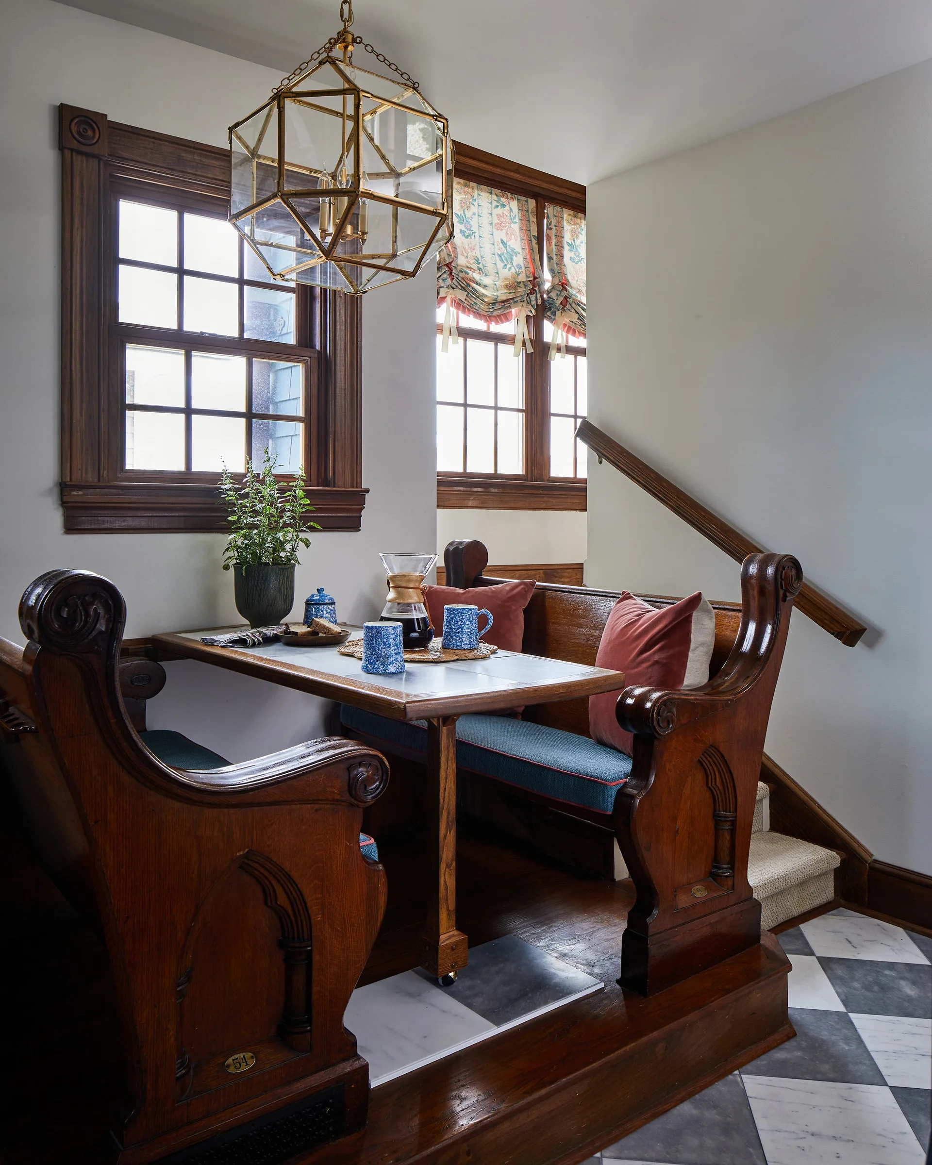 An eating nook with antique wooden church pews, a matching table, and a brass lantern pendant light on a checkerboard floor.