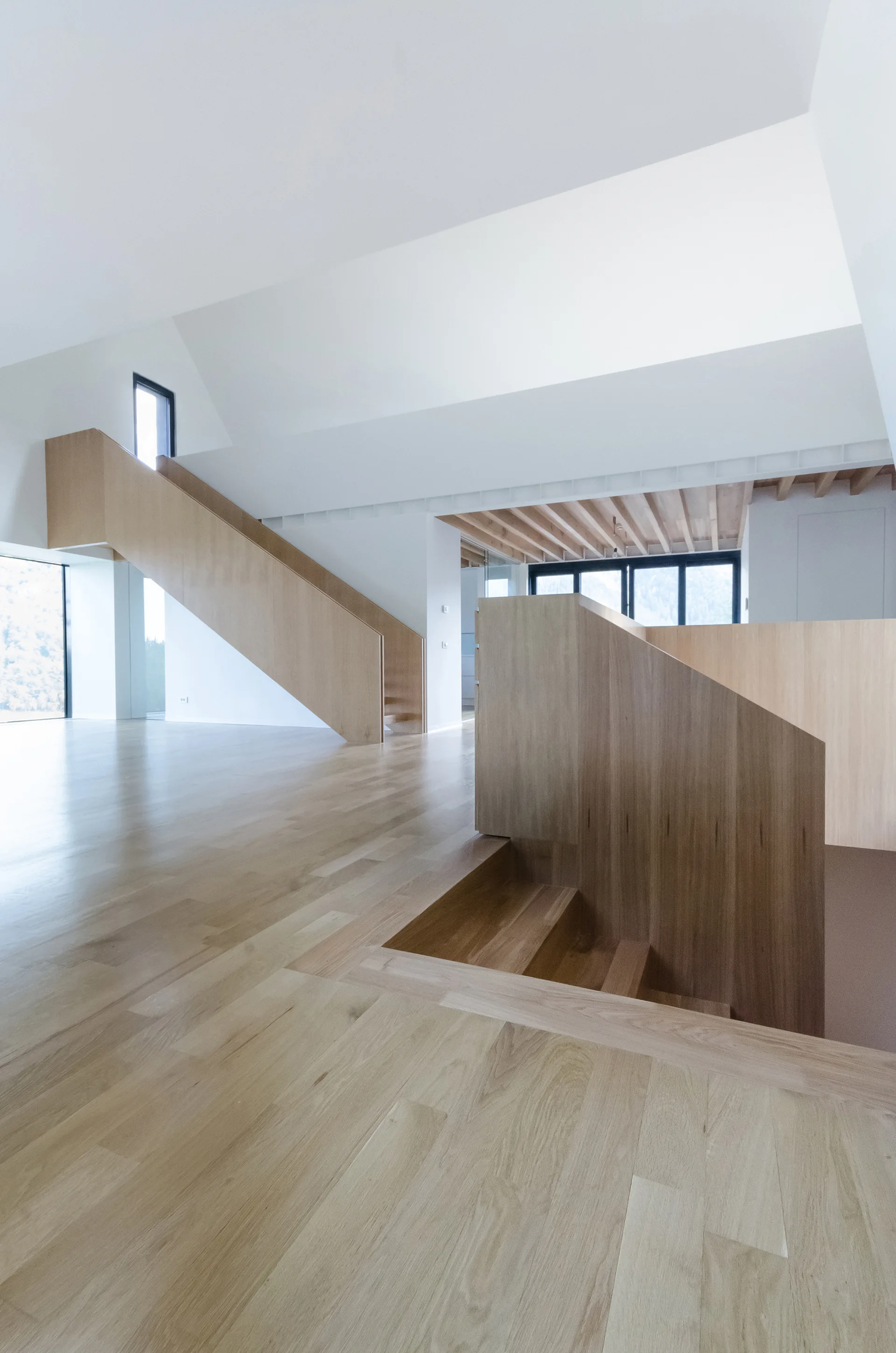 A modern minimalist interior featuring a solid light wood staircase and matching hardwood floors against clean white walls.