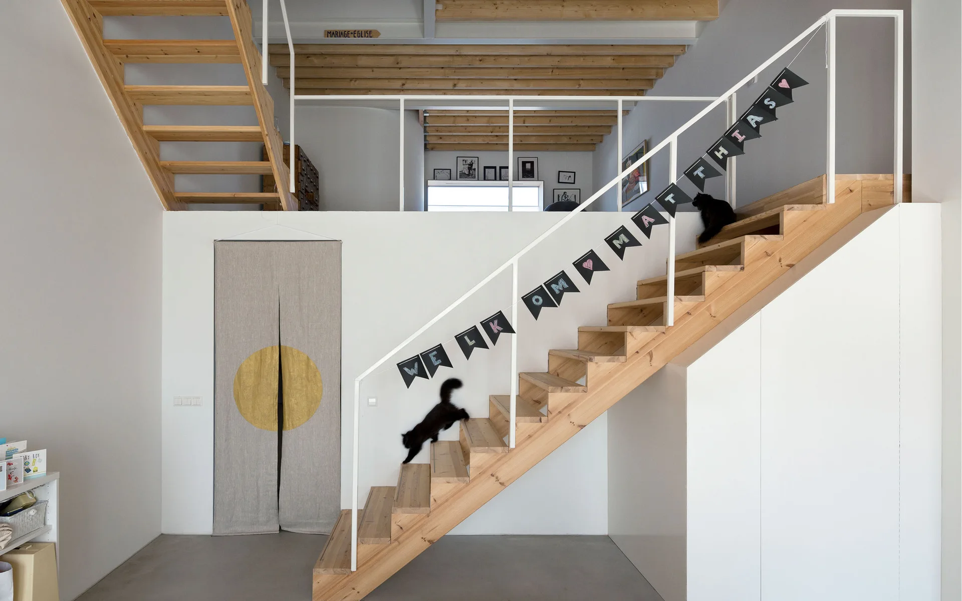 A minimalist wooden staircase with a white railing features integrated under-stair storage cabinets and leads to a mezzanine level.