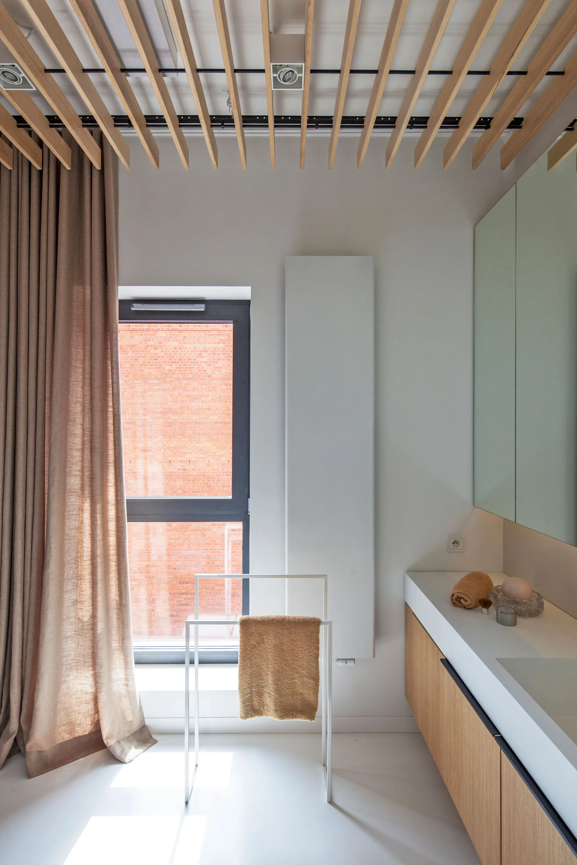 A modern minimalist bathroom with a wood slatted ceiling, a light wood vanity, and a tall white vertical radiator.