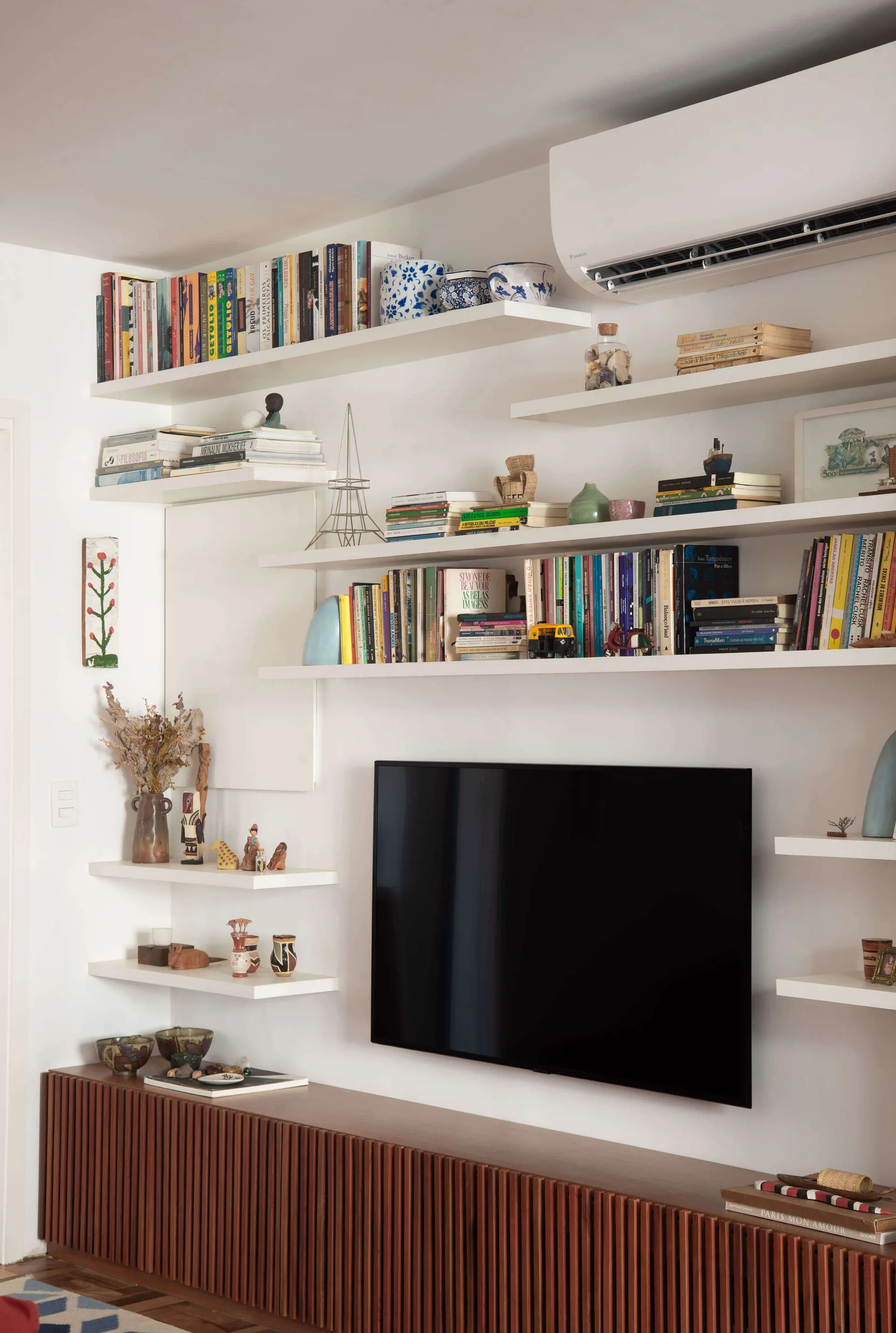 A wall-mounted television is framed by white floating bookshelves above a long, slatted dark wood media cabinet in a living room.