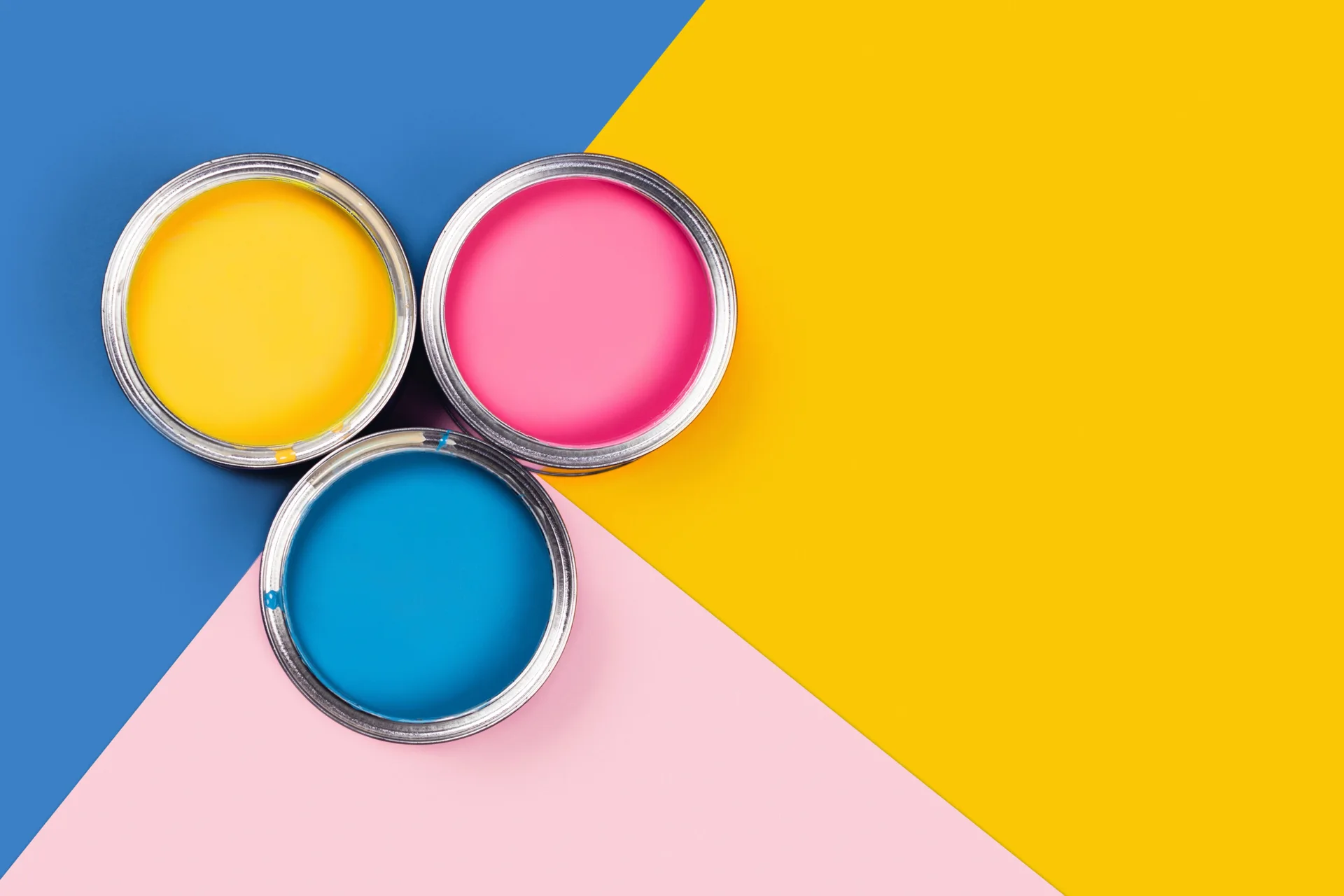 Three open metal paint cans filled with yellow, pink, and blue liquid paint are arranged on a matching geometric color-blocked background.