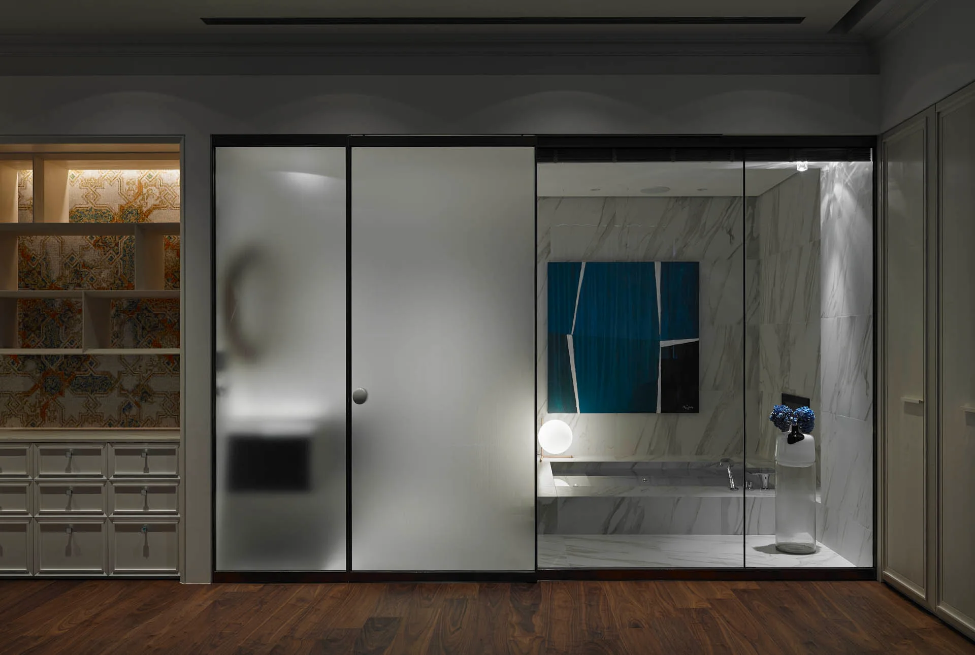 A contemporary bathroom wet area with veined marble walls is visible behind a sliding glass partition featuring both frosted and clear panels.