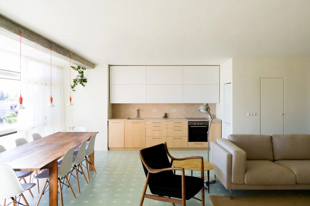 An open-concept living space features a pale blue patterned tile floor, a wood dining table, white kitchen cabinets, and a beige sofa.