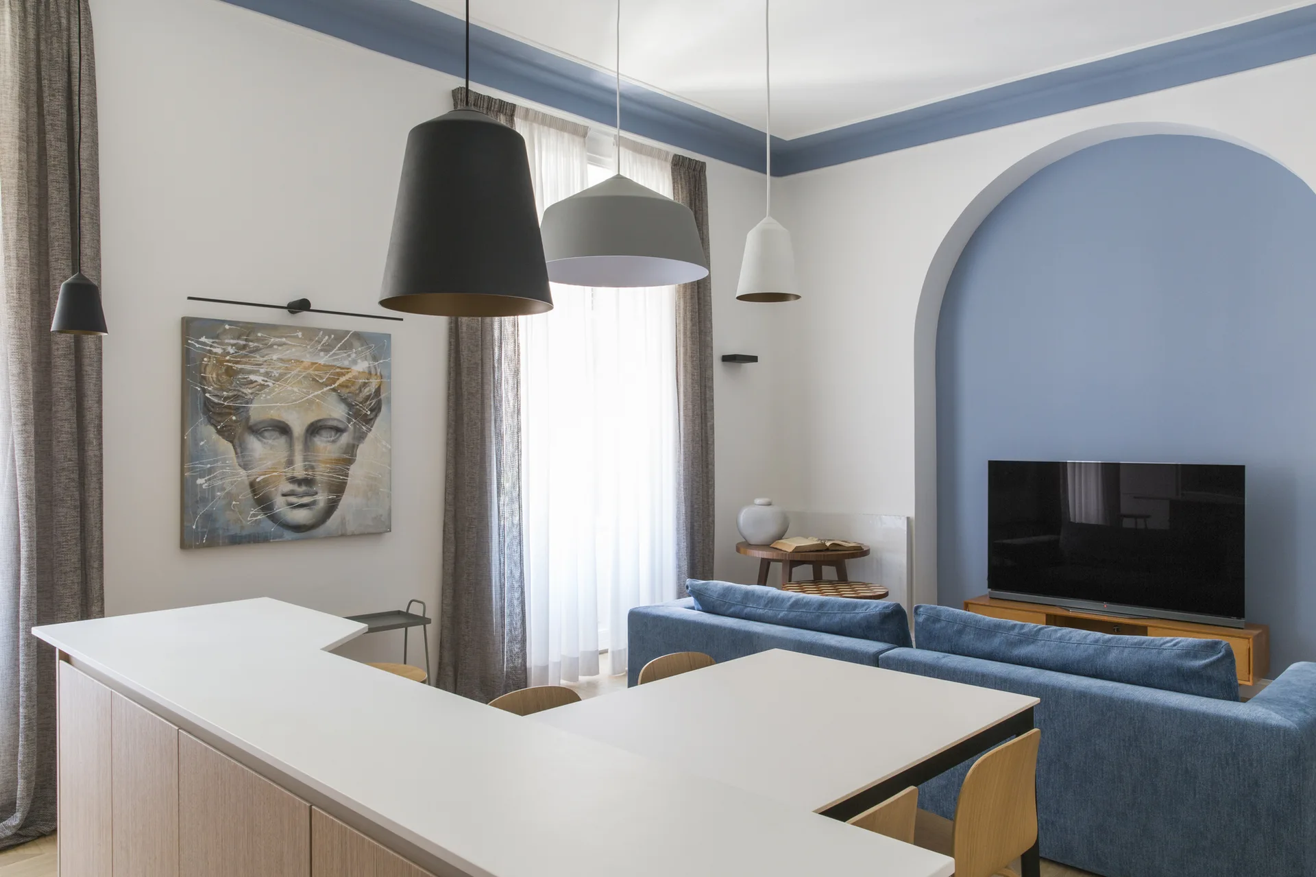 A contemporary living room features a blue sofa, three hanging pendant lights, and a matching blue painted arched niche behind a television.