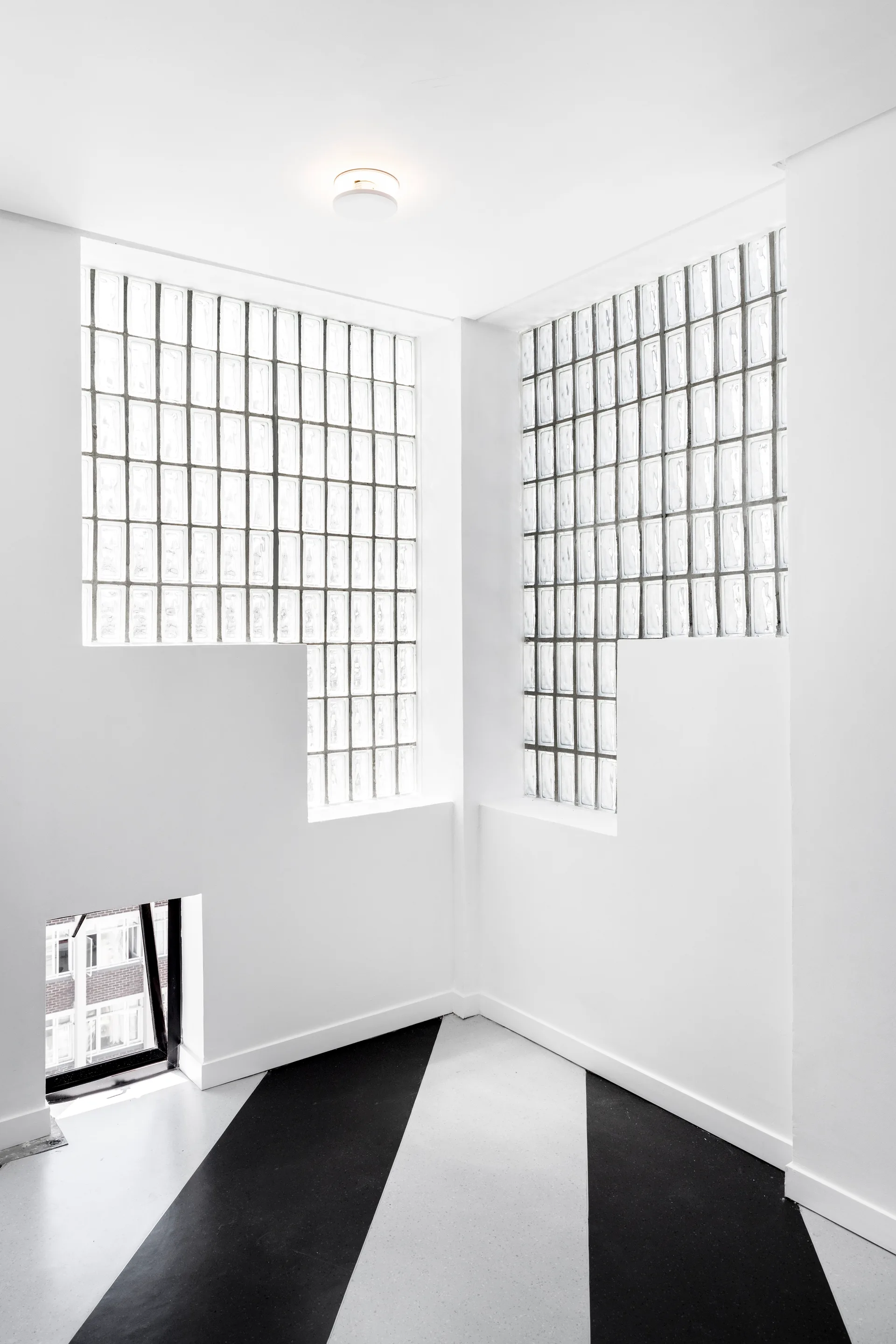An interior room corner features white walls with integrated glass block windows and a floor with bold black and white diagonal stripes.