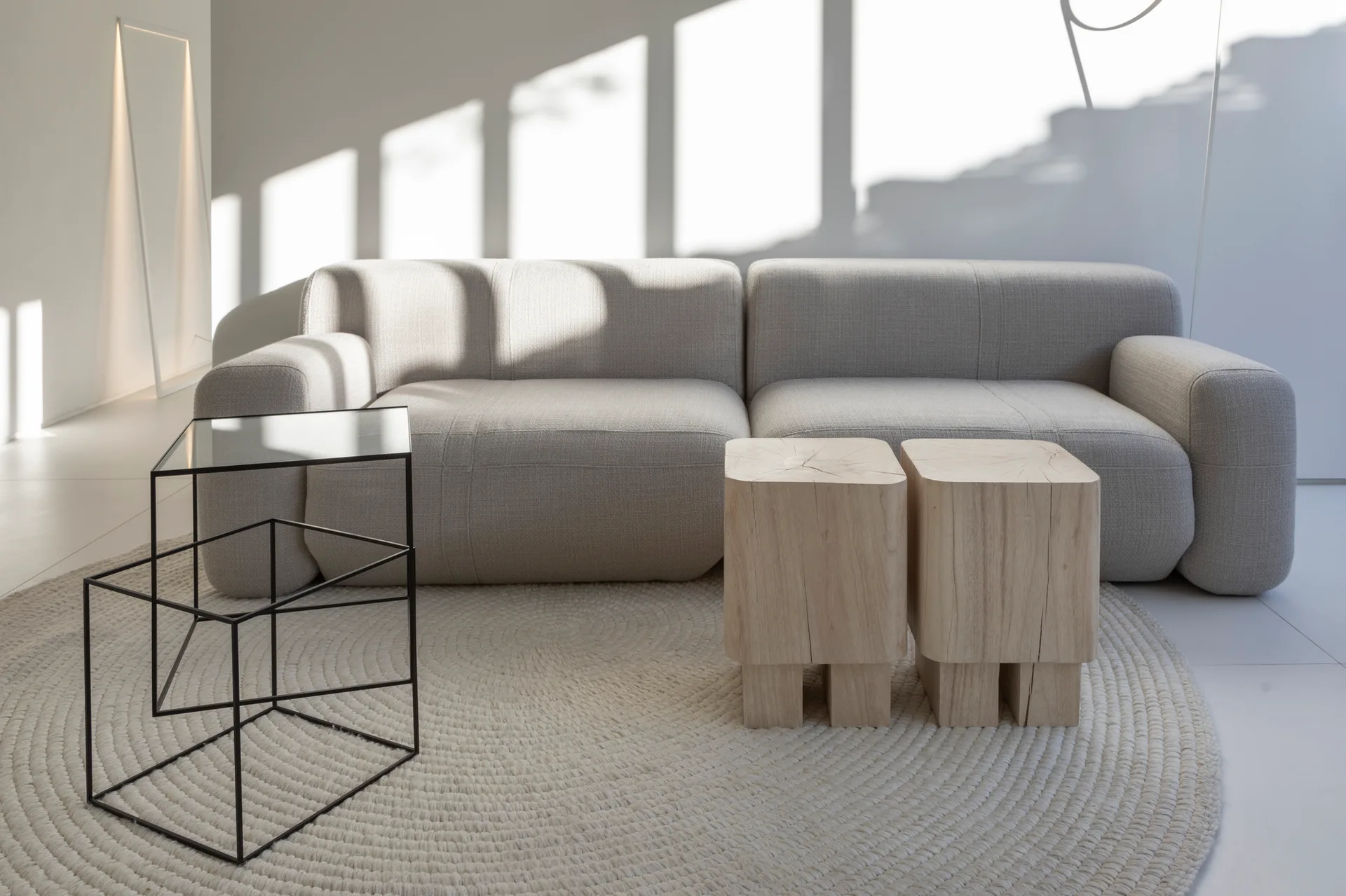 A light grey modular sofa sits on a round woven rug next to two raw wood block stools and a black metal side table.