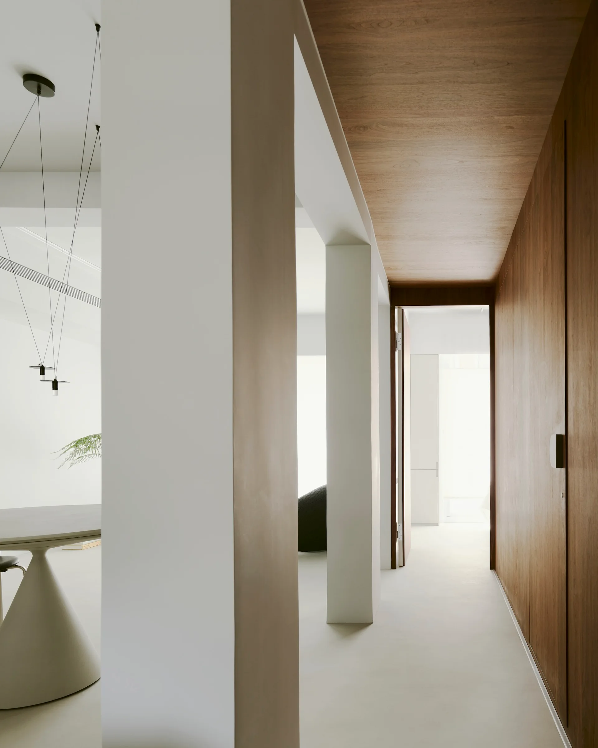 A modern interior corridor with smooth white columns, a circular pedestal table, and a hallway featuring a warm wood paneled wall and ceiling.