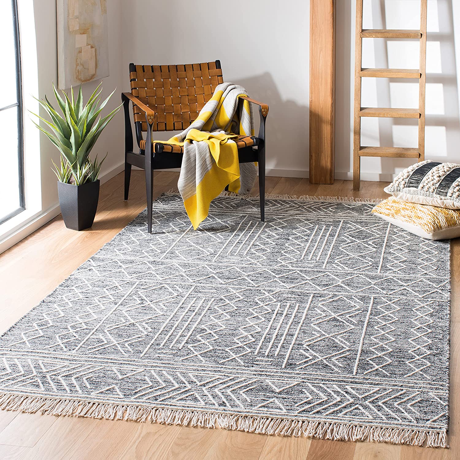 A woven leather accent chair with a yellow throw blanket sits on a large geometric patterned grey rug next to a decorative wooden ladder.