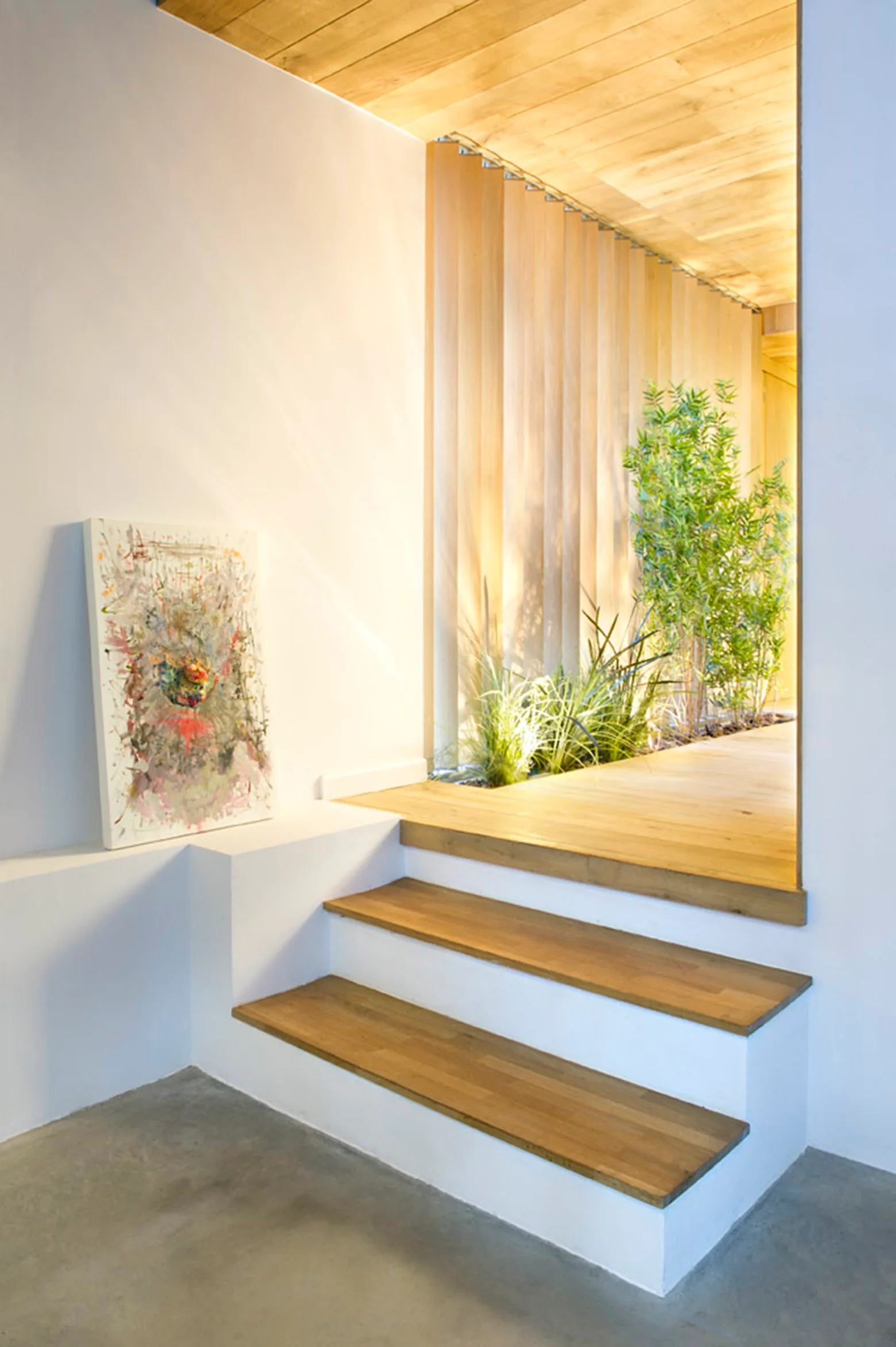 A modern entryway featuring white and wood stairs leading to a platform with a vertical slat wall, integrated green plants, and a wood ceiling.