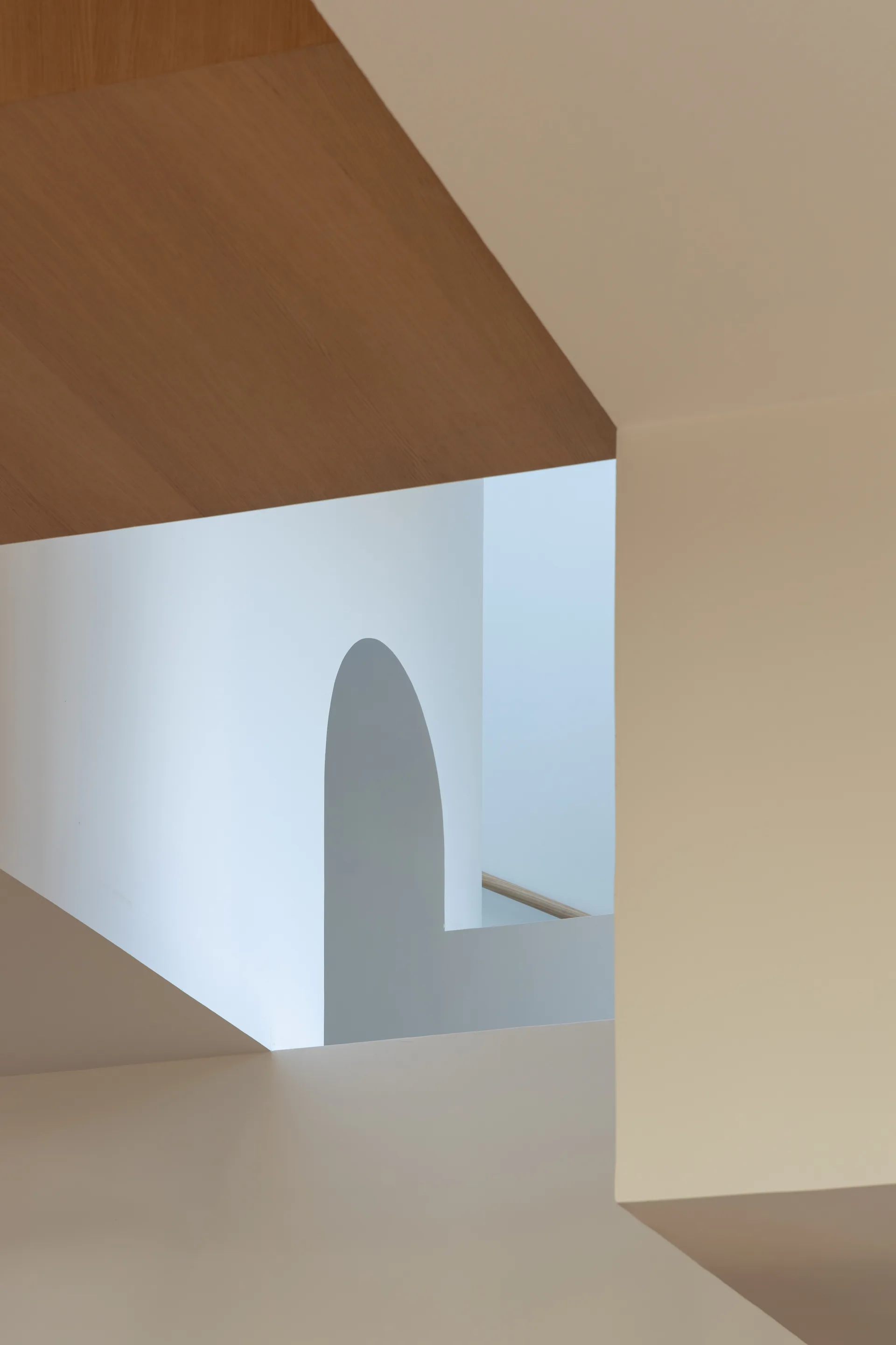 Architectural detail of a modern stairwell with geometric white wall cutouts, an internal archway, and a light wood ceiling plane.
