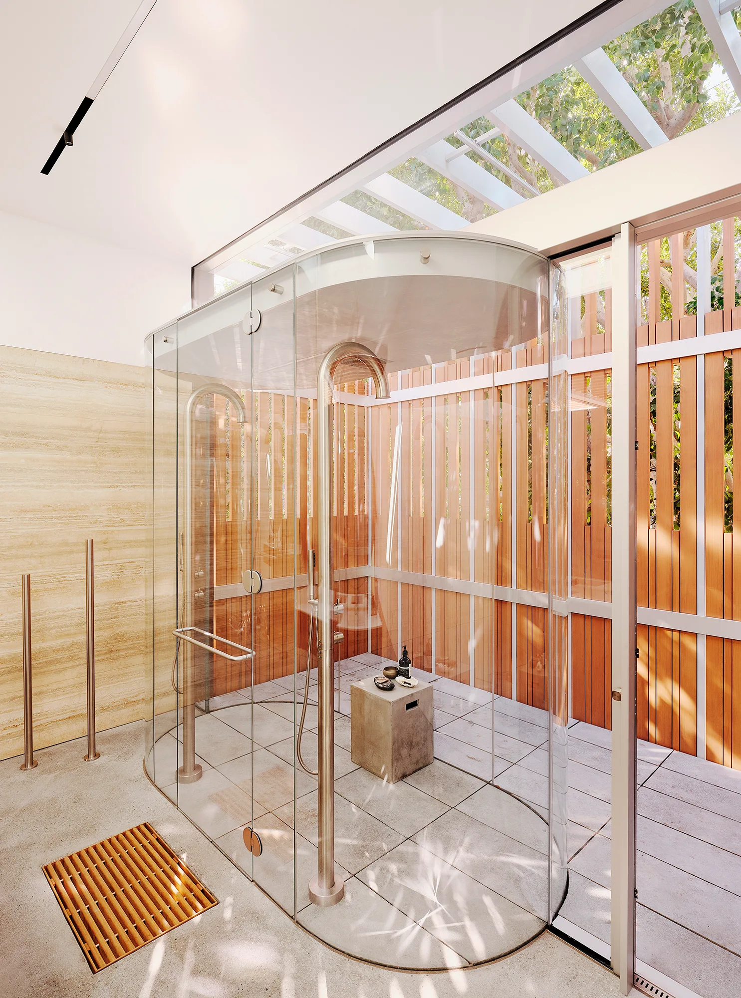 A modern bathroom features a curved glass shower enclosure with metal fixtures, surrounded by slatted wood walls and a skylight ceiling.