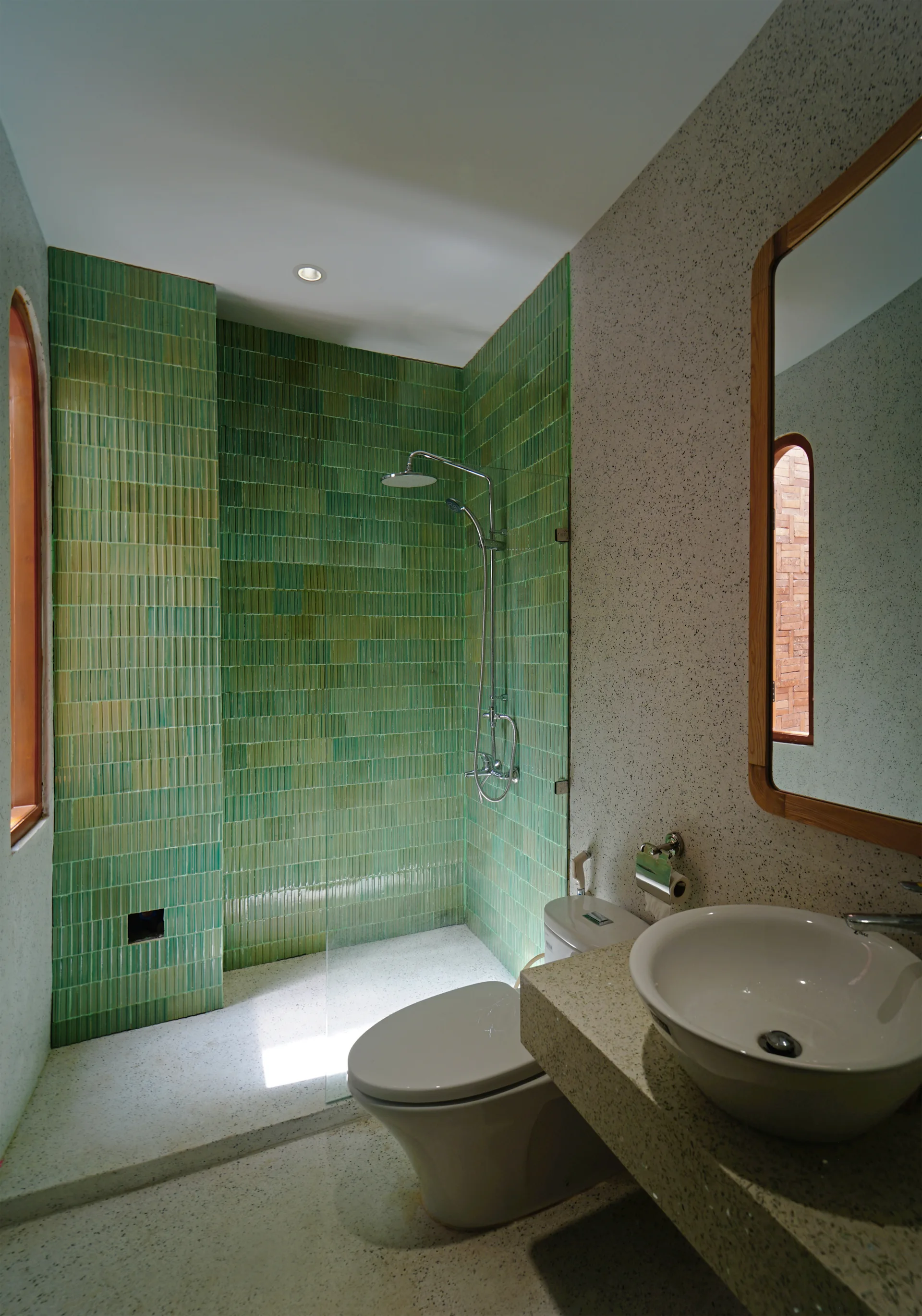 A contemporary bathroom features a shower enclosed in vertical green tiles, a white toilet, and a vessel sink resting on a speckled grey stone vanity.