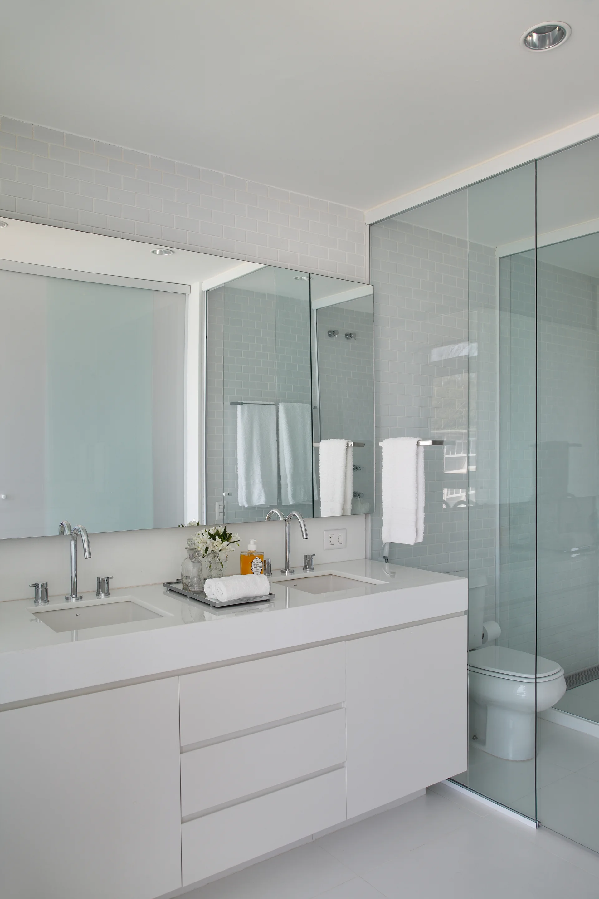 A bright modern bathroom featuring a white floating double vanity, polished chrome faucets, a large mirror, and a glass-enclosed shower.