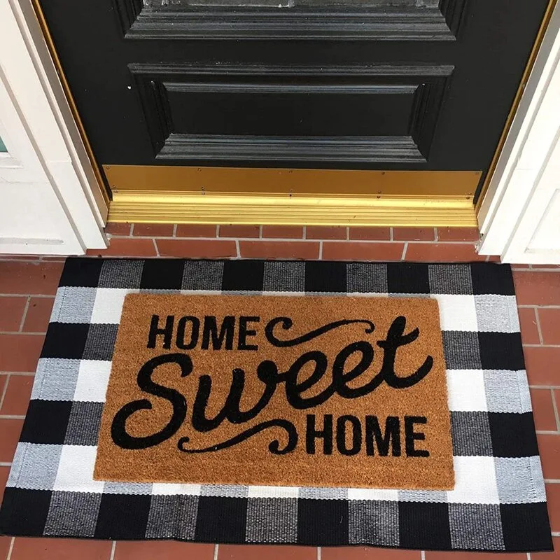 A black front door with a gold threshold is accented by a layered buffalo check rug and a natural coir doormat.