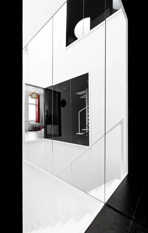 A high-contrast minimalist staircase features white steps and railings alongside tall glass partitions and reflective black wall paneling.