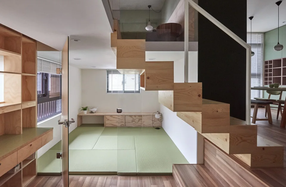 A minimalist split-level room with a floating wood staircase, green tatami mat flooring, and light wood plywood shelving.
