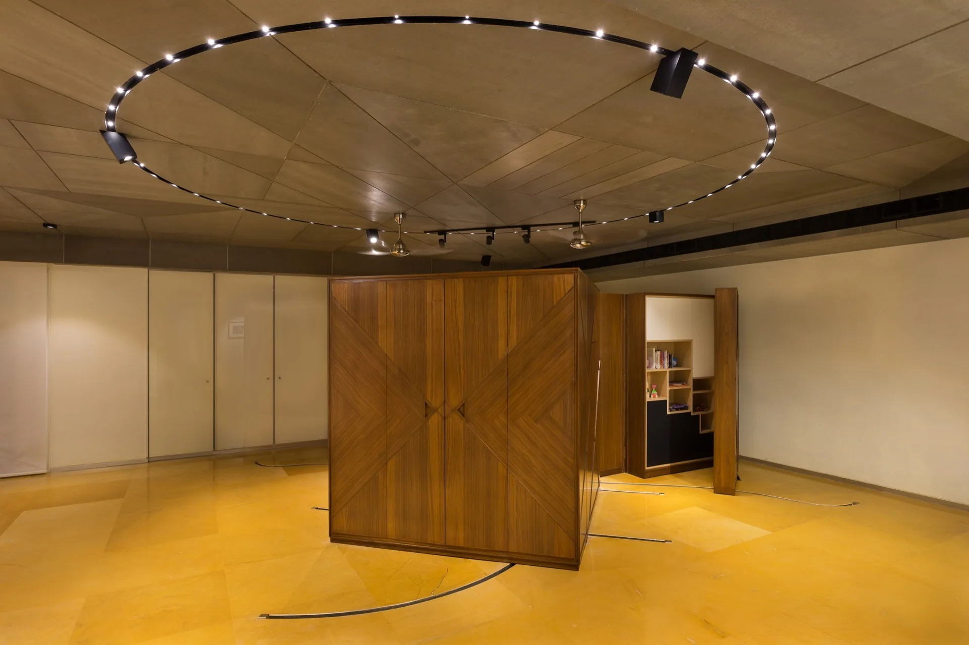 A large wooden cabinet with diagonal grain veneer stands on a yellow tiled floor beneath a circular track lighting system.