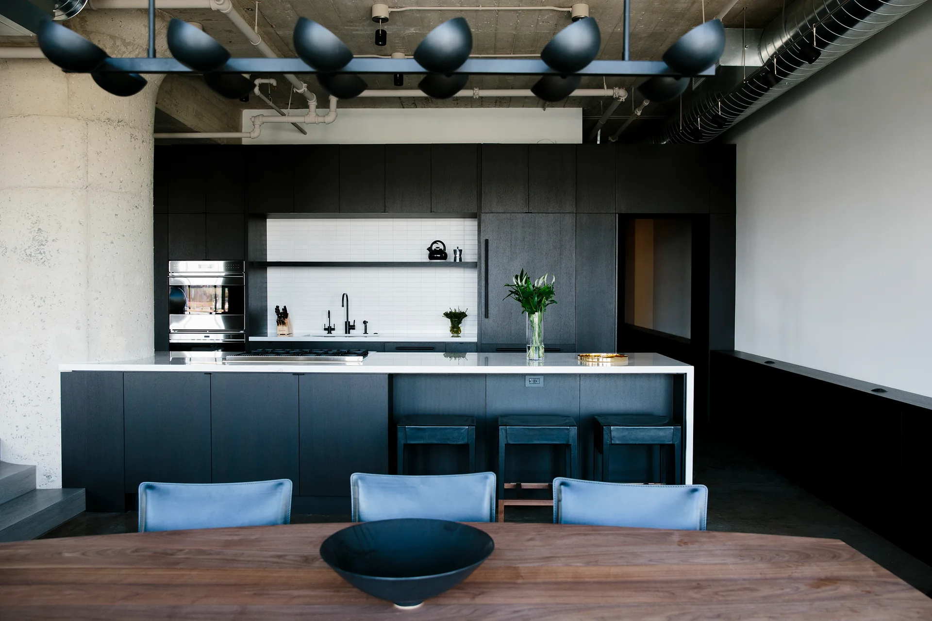 An industrial style kitchen with dark wood cabinetry, a white island, and exposed concrete ceilings.