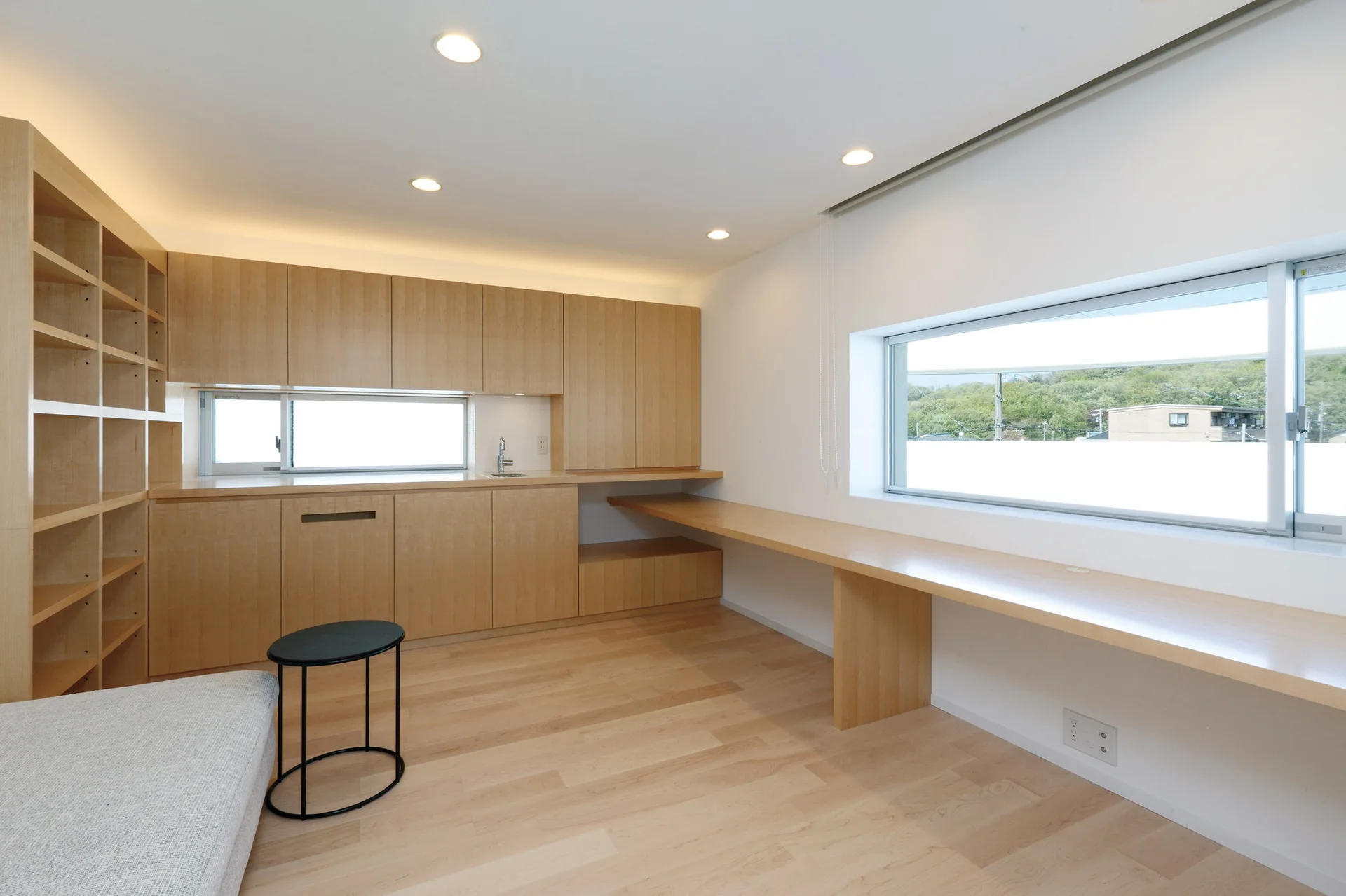 A minimalist home office with a custom light wood built-in desk under a horizontal window, surrounded by matching wooden cabinetry.
