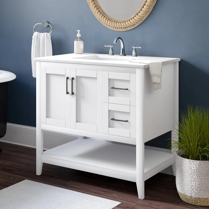 A white bathroom vanity with dark metal handles stands against a dark blue wall below a round mirror framed in woven rope.