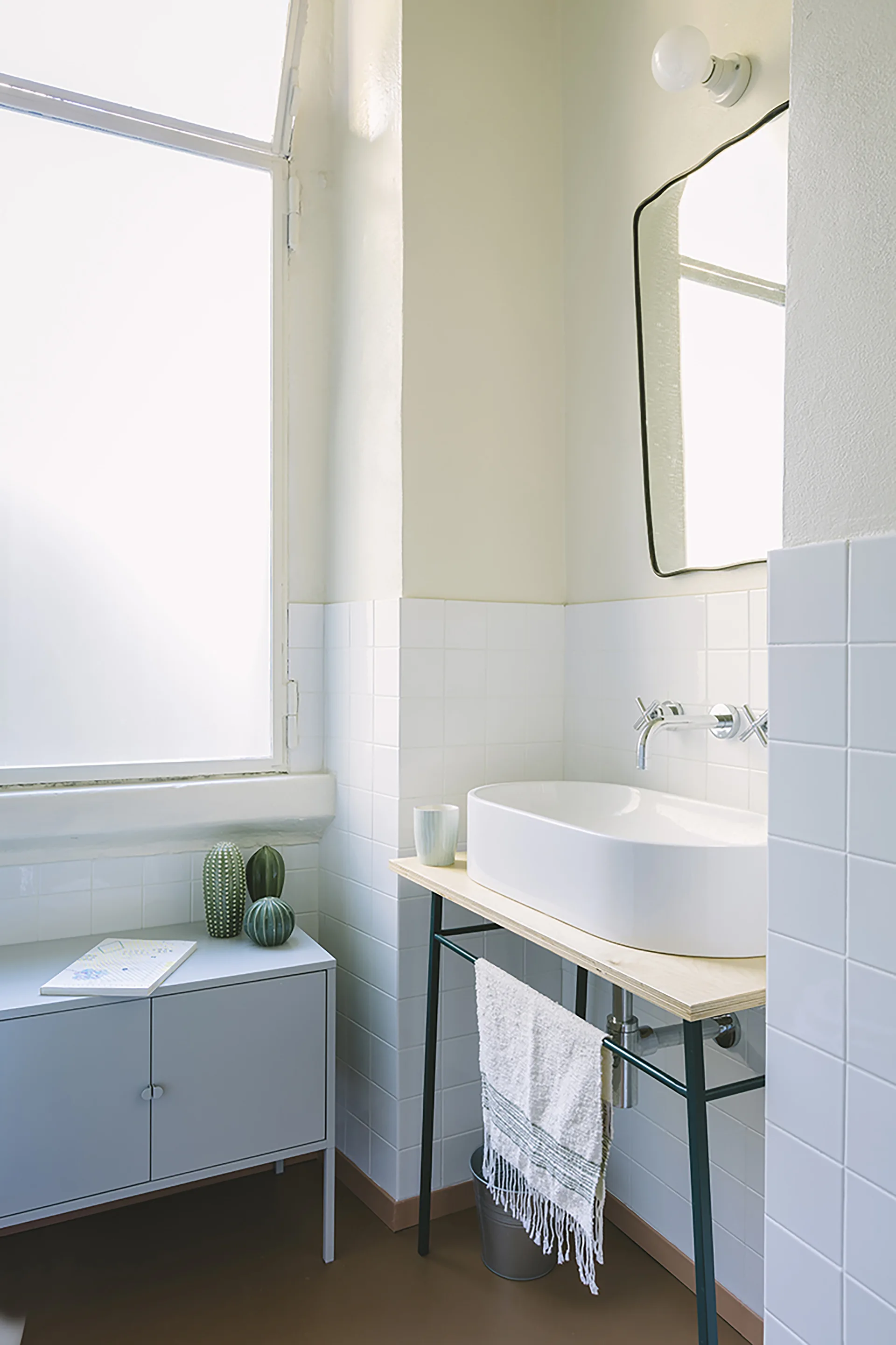 A minimalist bathroom features a white vessel sink on a wood-topped vanity against white square-tiled walls.