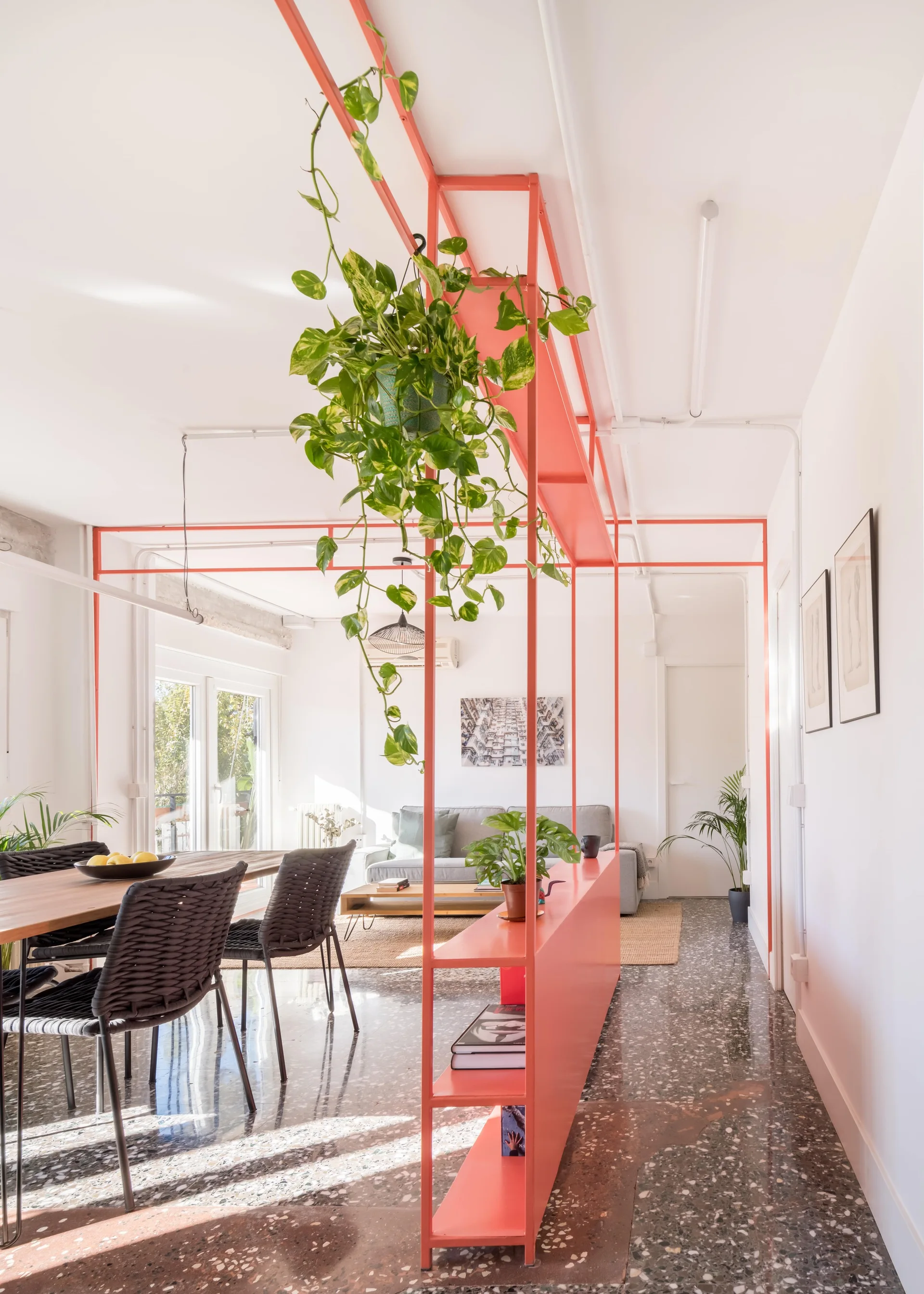 An open-concept living and dining area featuring a coral metal room divider, a wooden dining table, and dark speckled terrazzo flooring.