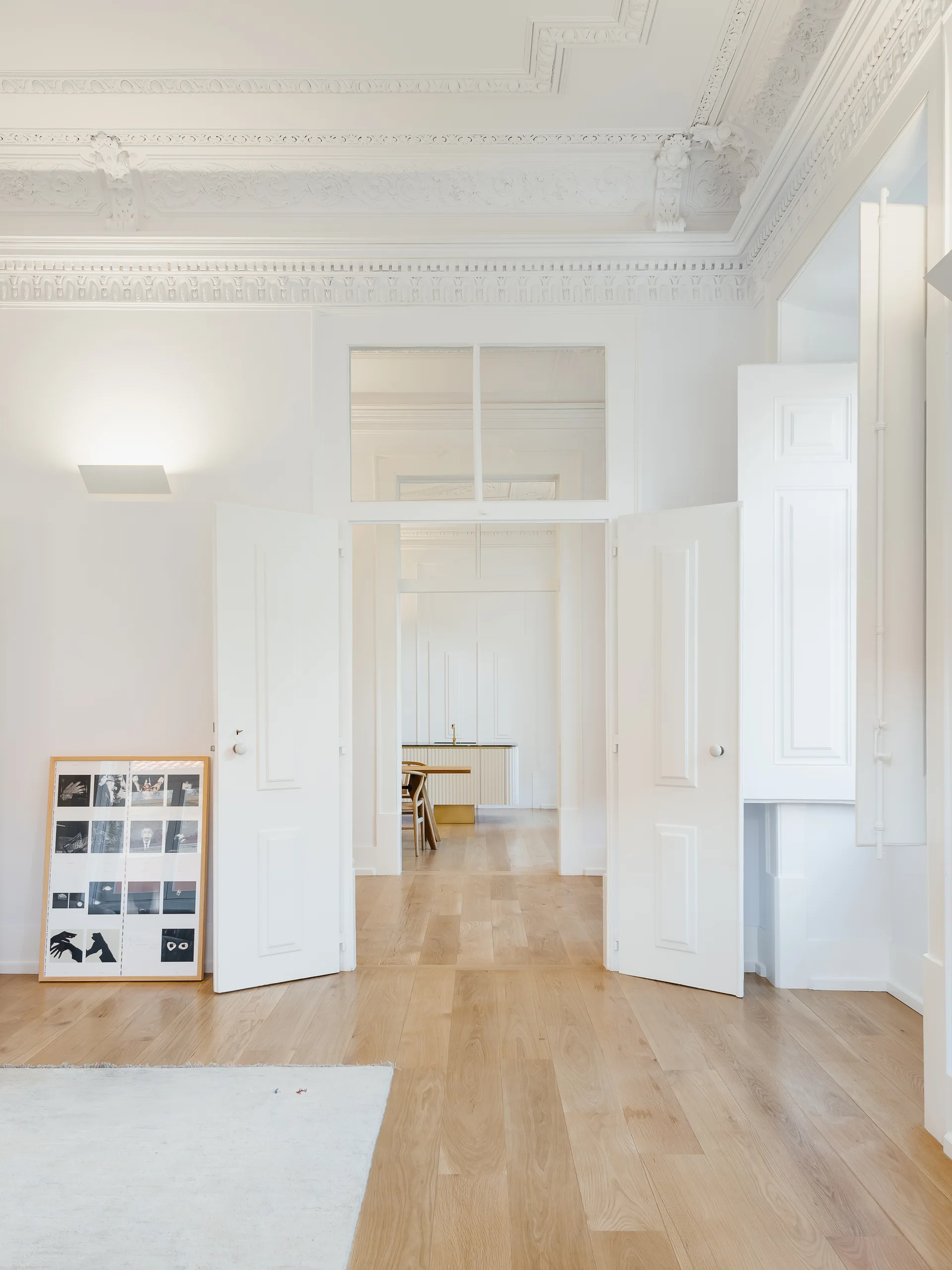 An enfilade of white double doors opens into consecutive rooms of a historic apartment featuring light wood floors and ornate plaster crown molding.
