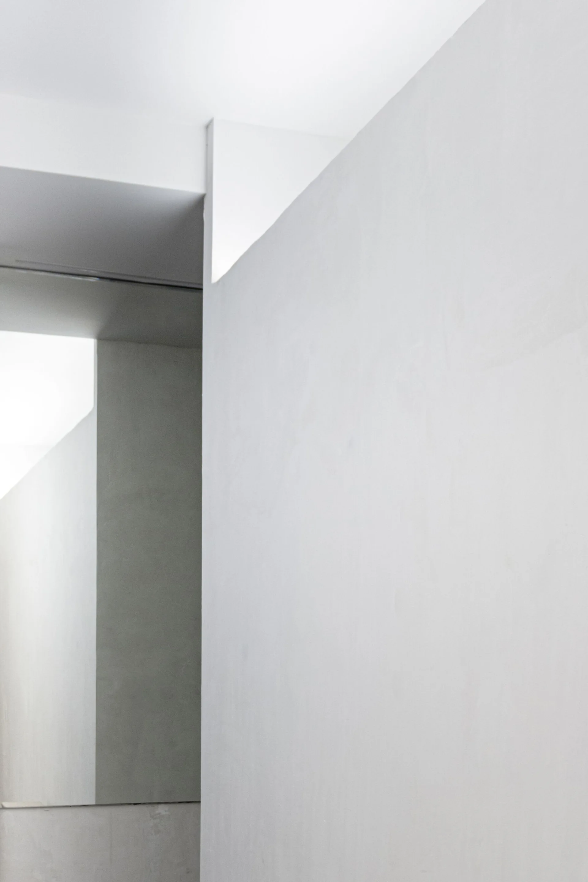 Clean white plaster walls meet at sharp geometric angles under diffused bright lighting in a minimalist interior space.