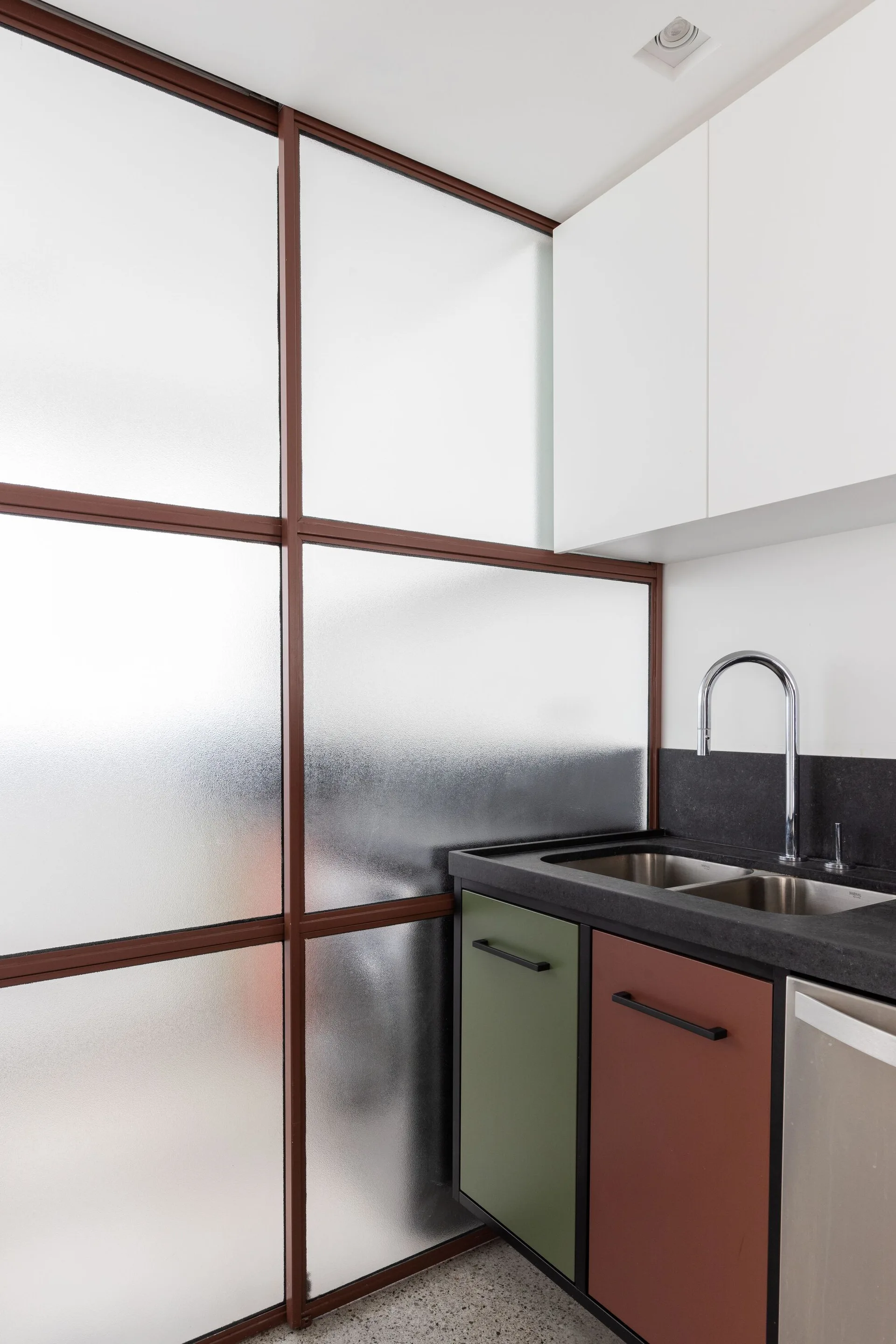 A kitchen corner features a frosted glass partition with a brown frame next to green and reddish-brown base cabinets under a dark countertop.