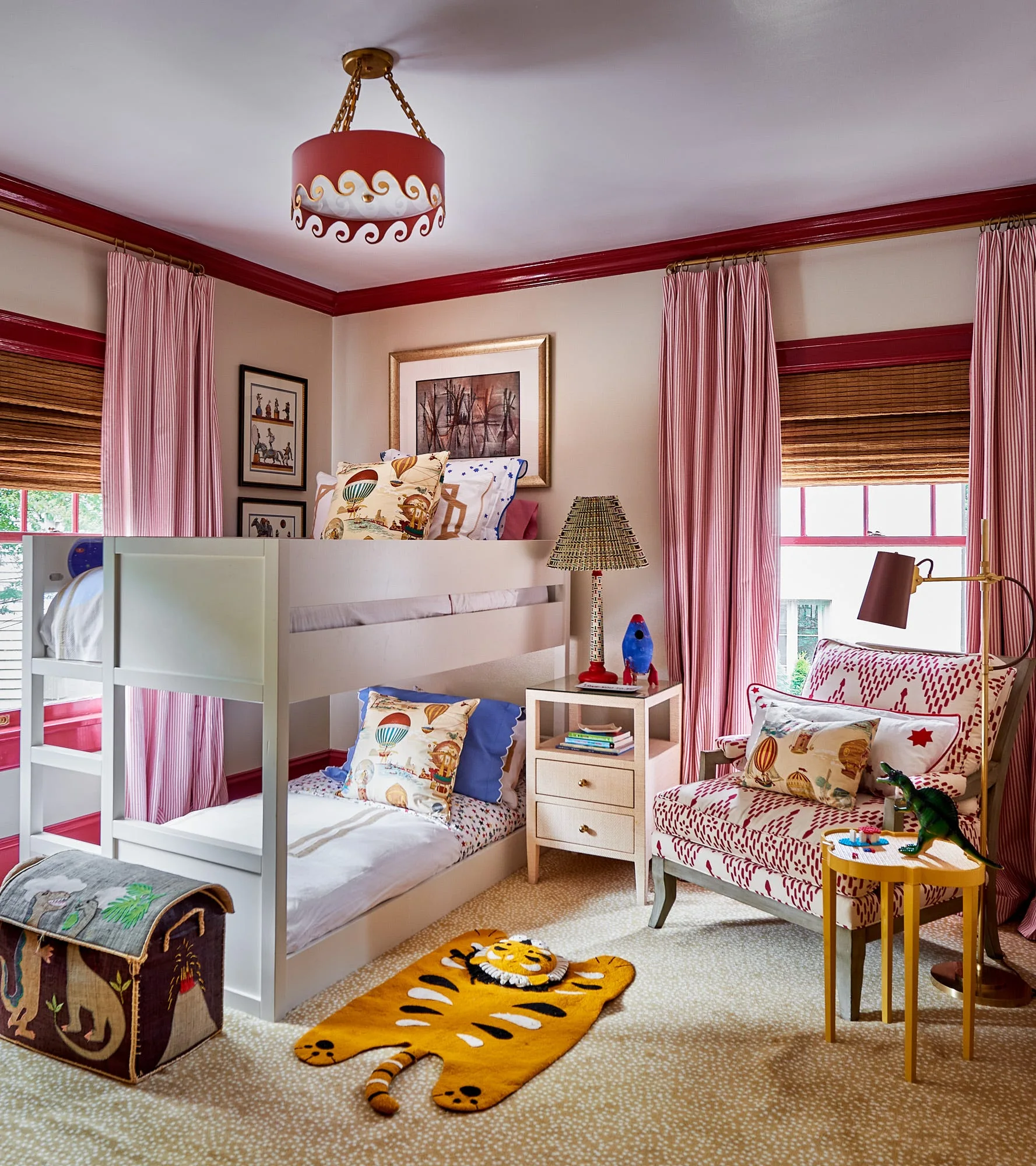 A children's bedroom features a white wood bunk bed, a red patterned armchair, pink striped curtains, and bold red crown molding along the ceiling.