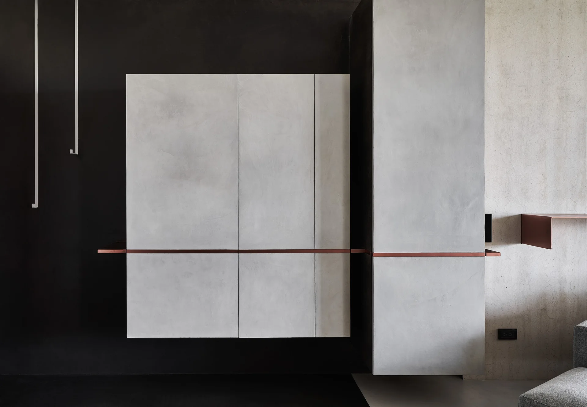 A light gray minimalist floating cabinet is mounted on a matte black wall and accented by a thin horizontal copper trim piece.
