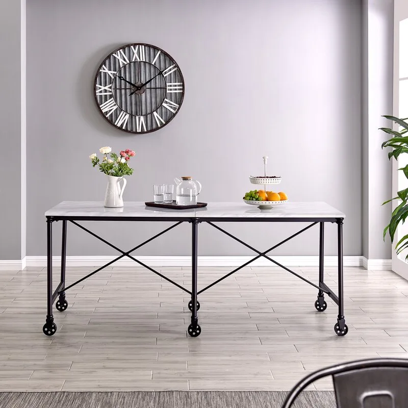 A rectangular white marble-topped dining table with a black industrial metal frame on caster wheels sits against a plain light gray wall with a round clock.